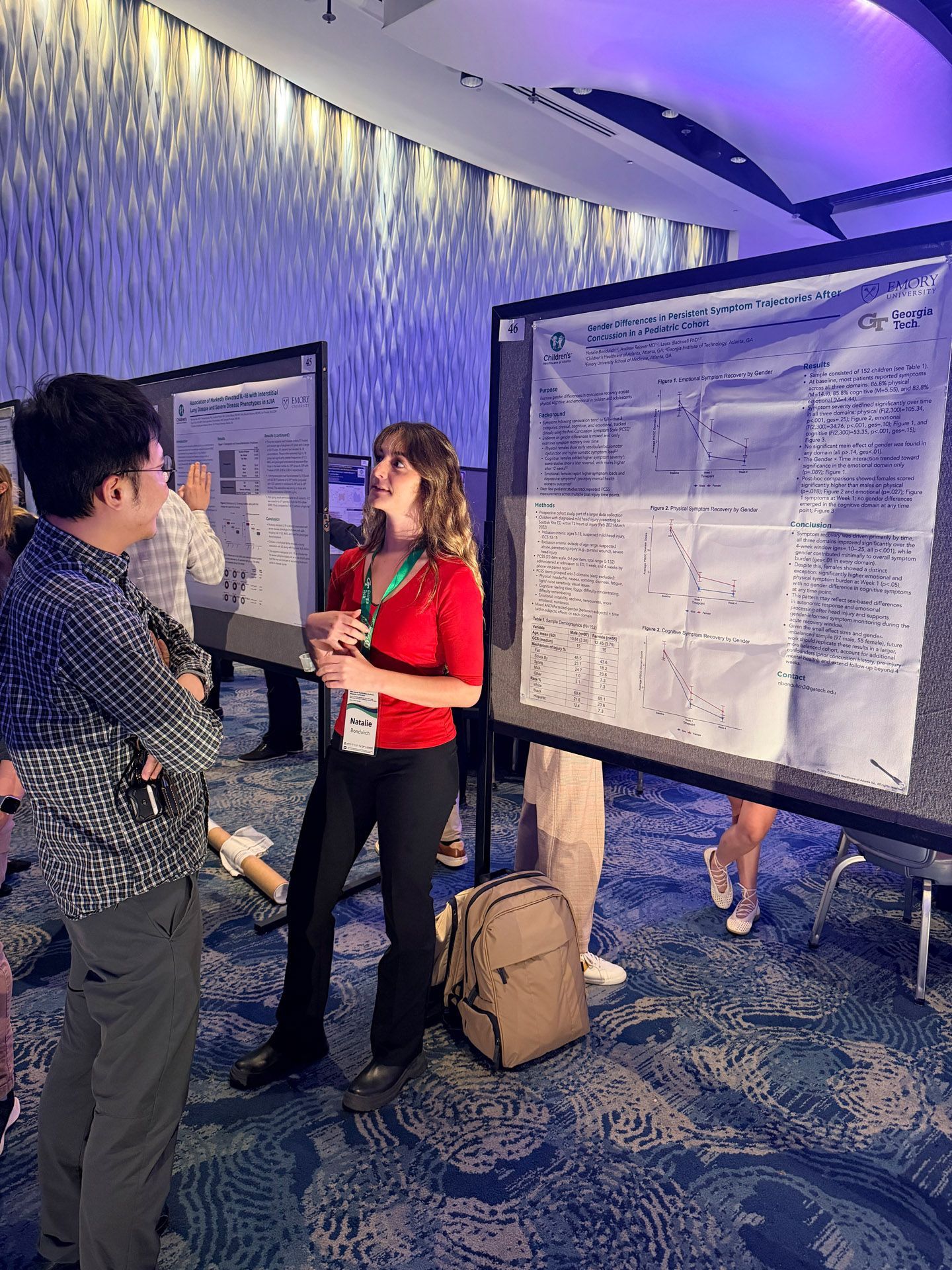 People viewing research posters at a conference, with a woman in red presenting beside a poster board.