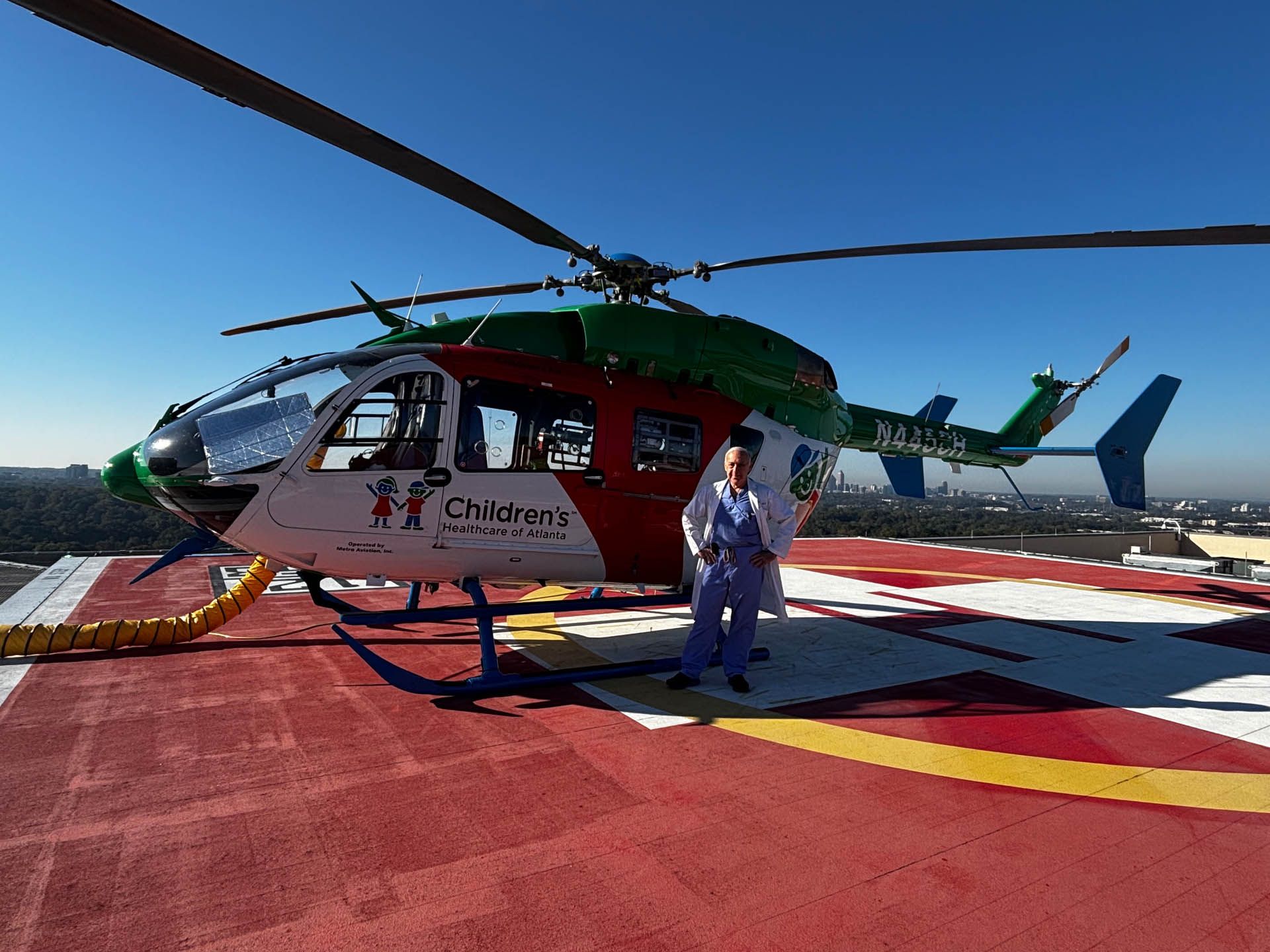 Helicopter on a helipad with a person standing beside it under a clear blue sky