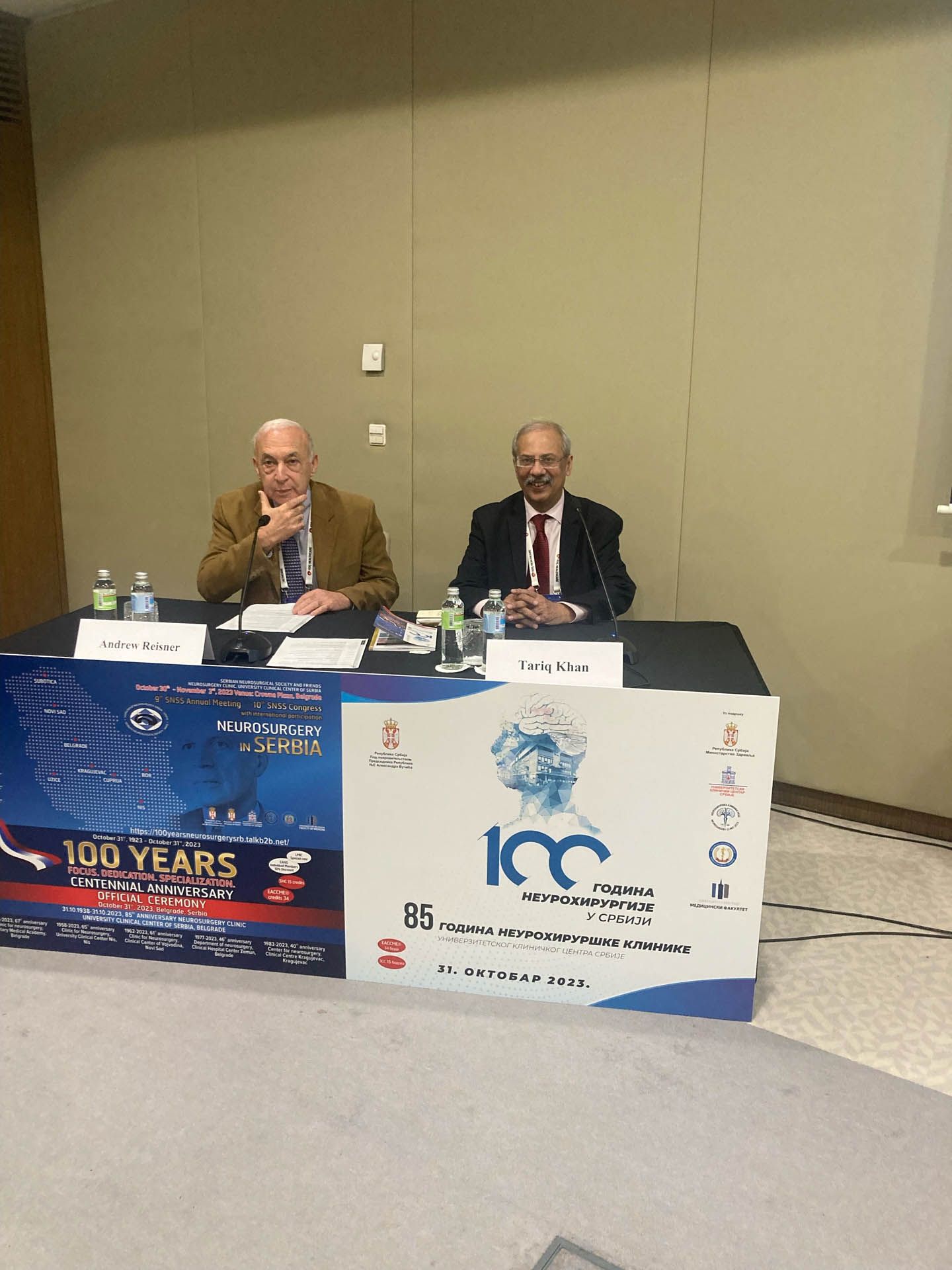 Two men are sitting at a table in front of a sign that says 100 years.
