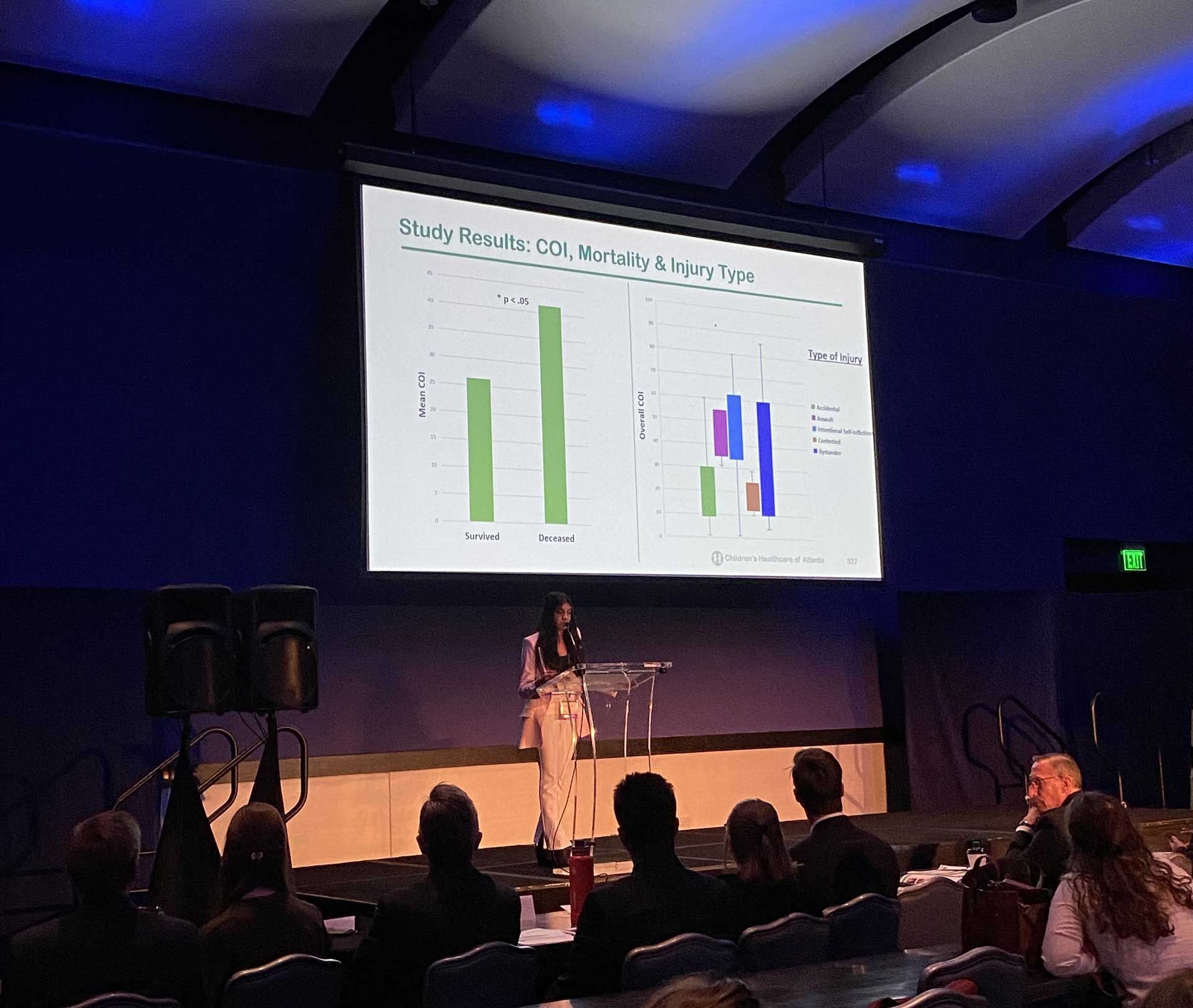 A presenter stands at a podium, presenting a graph to an audience in a conference setting.