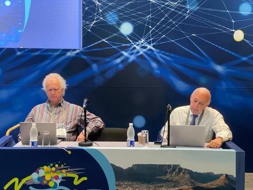 Two men are sitting at a table with laptops and microphones. Two men are sitting at a table with laptops and microphones.