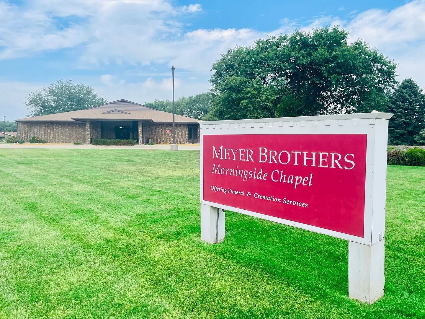 Meyer Brothers Colonial Chapel sign in a grassy field with a stone building and trees in the background