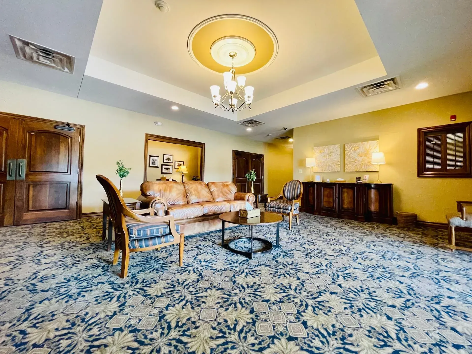Elegant living room with blue patterned carpet, beige sofa, chandelier, and dark wood furniture