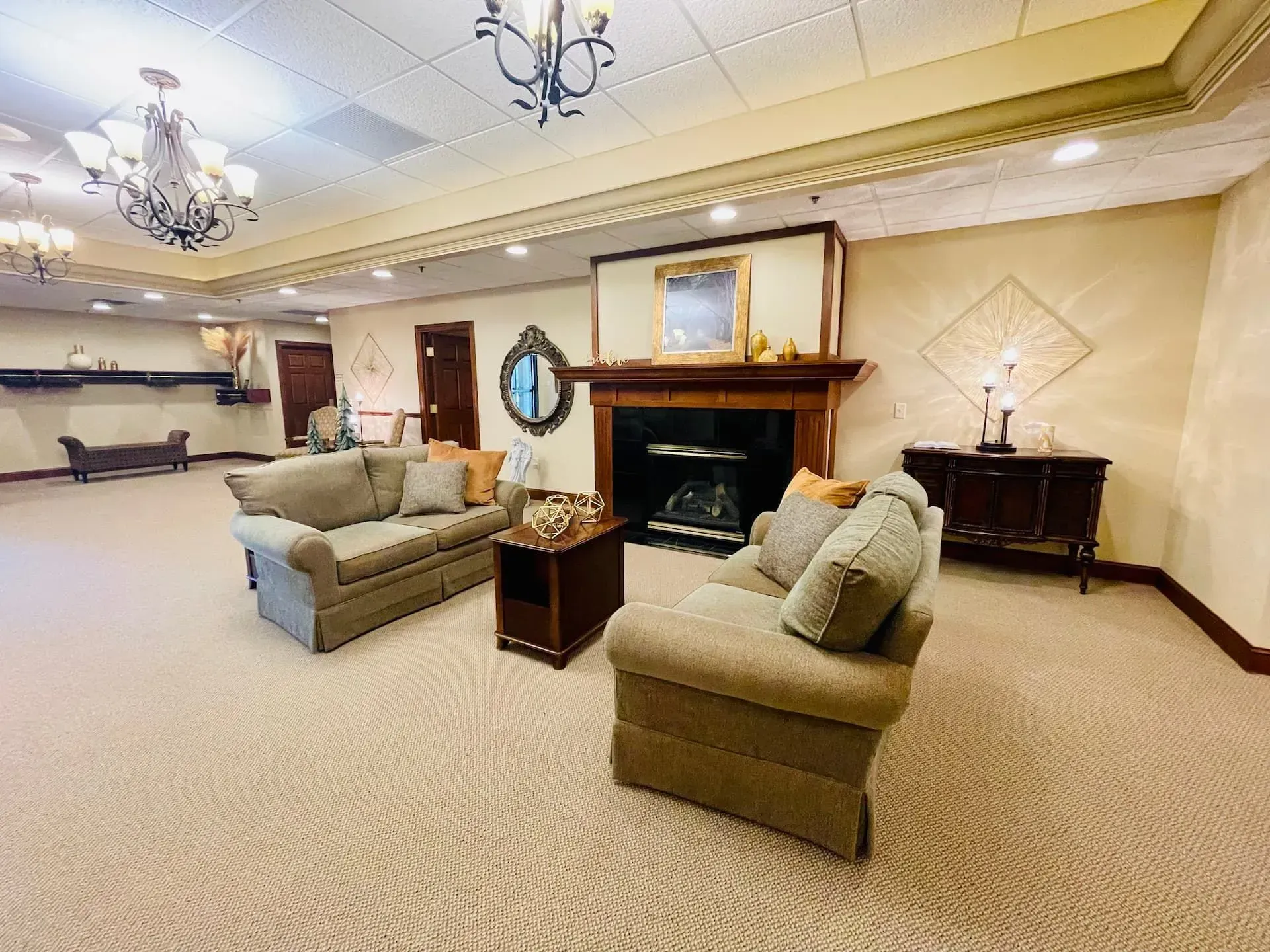 Spacious beige lobby with sofas, fireplace, chandeliers, and a side table