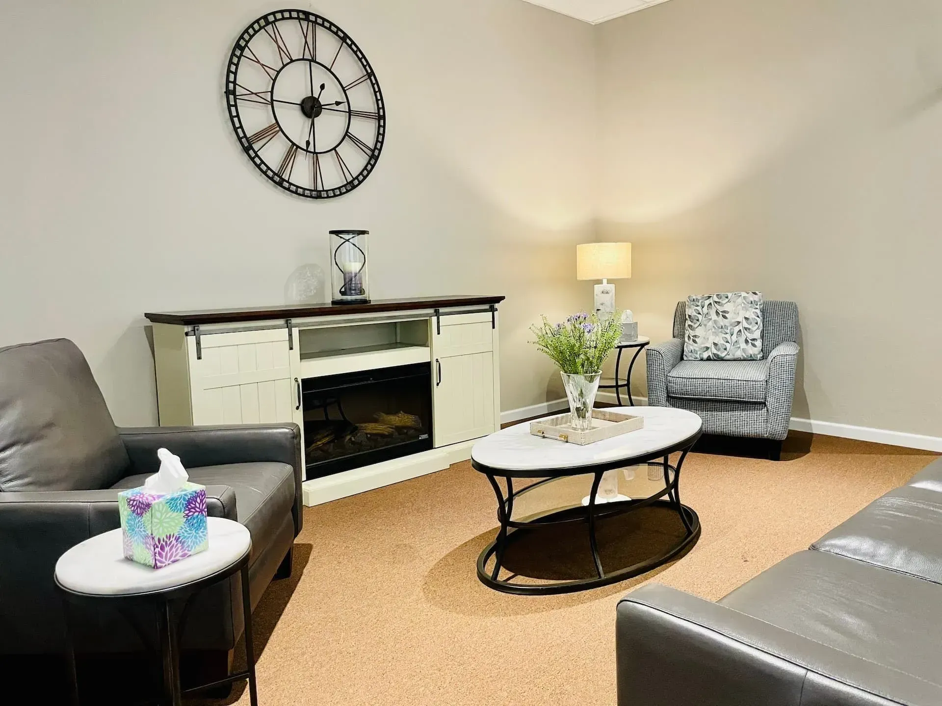Cozy living room with fireplace, wall clock, gray seating, and a white coffee table.