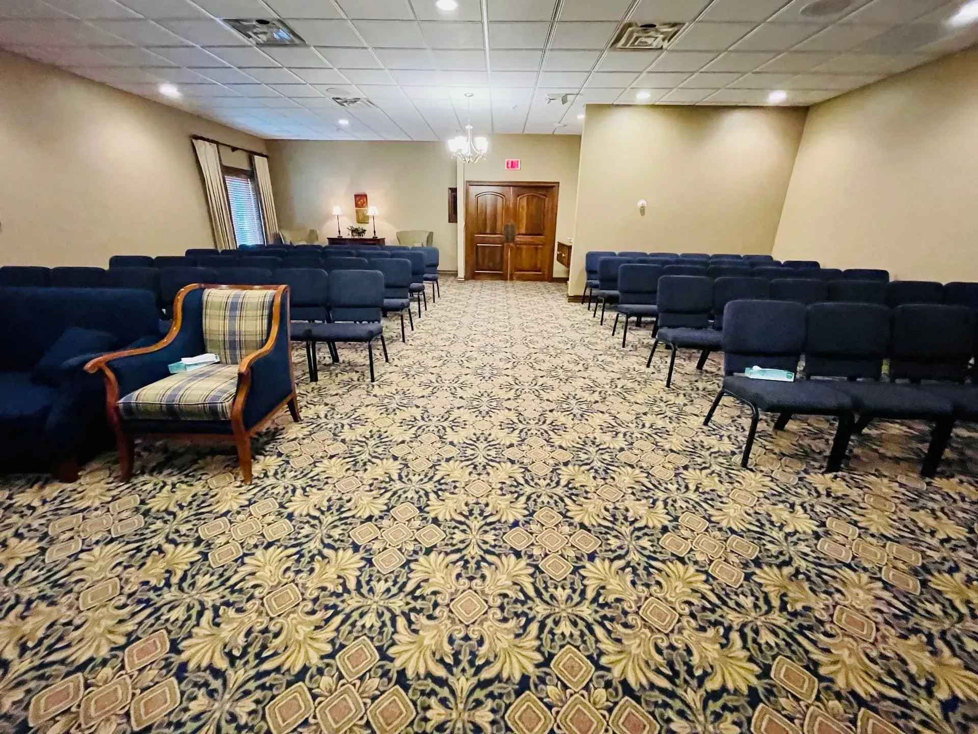 Empty meeting room with blue chairs, patterned carpet, and double wooden doors at the far end