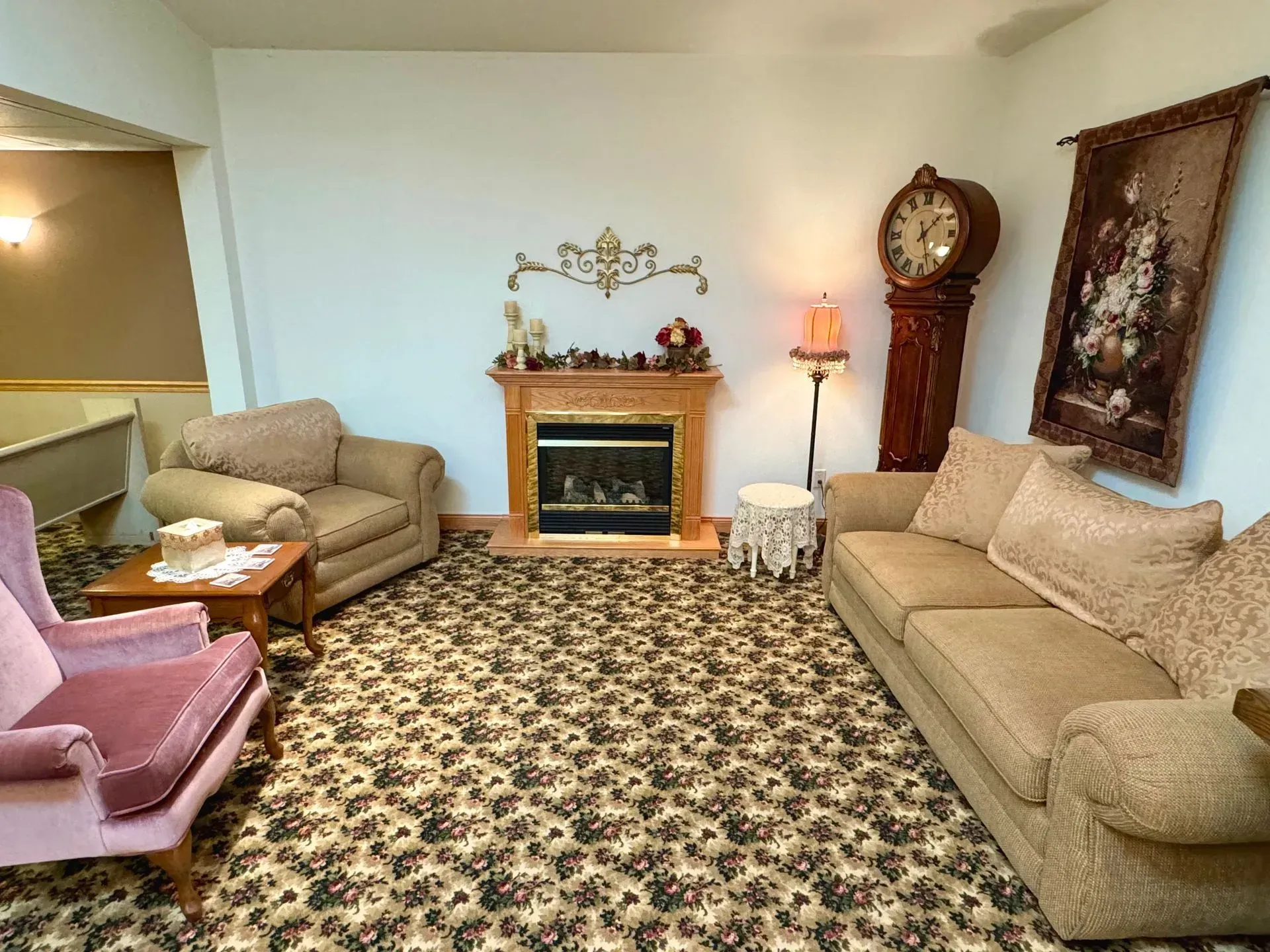 Living room with beige sofas, patterned rug, fireplace, lamp, and ornate wall decor