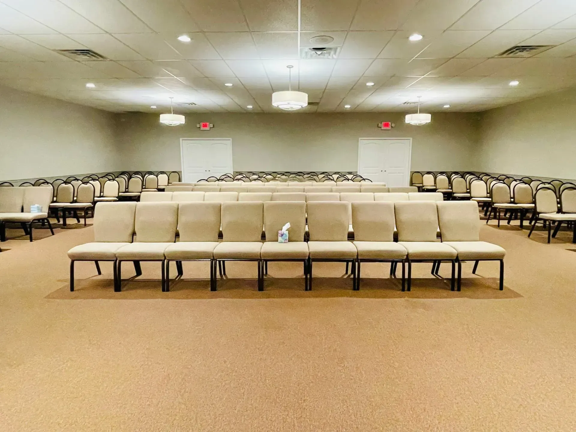 Empty auditorium with rows of beige chairs and a central aisle under ceiling lights.