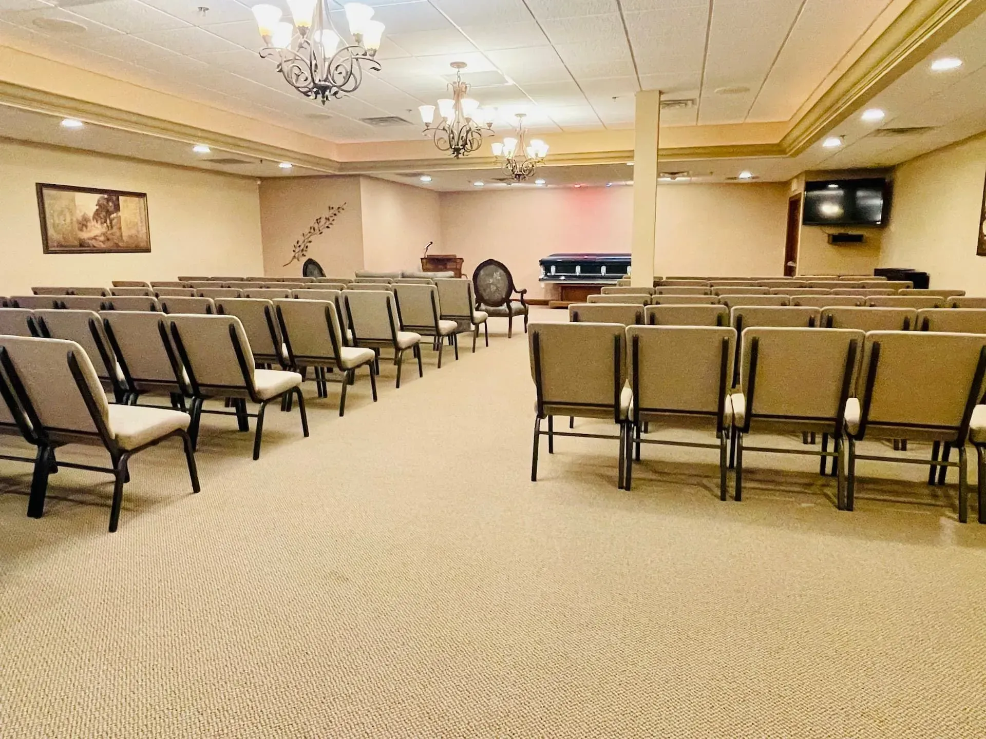Empty conference room with rows of beige chairs and chandeliers under warm lighting