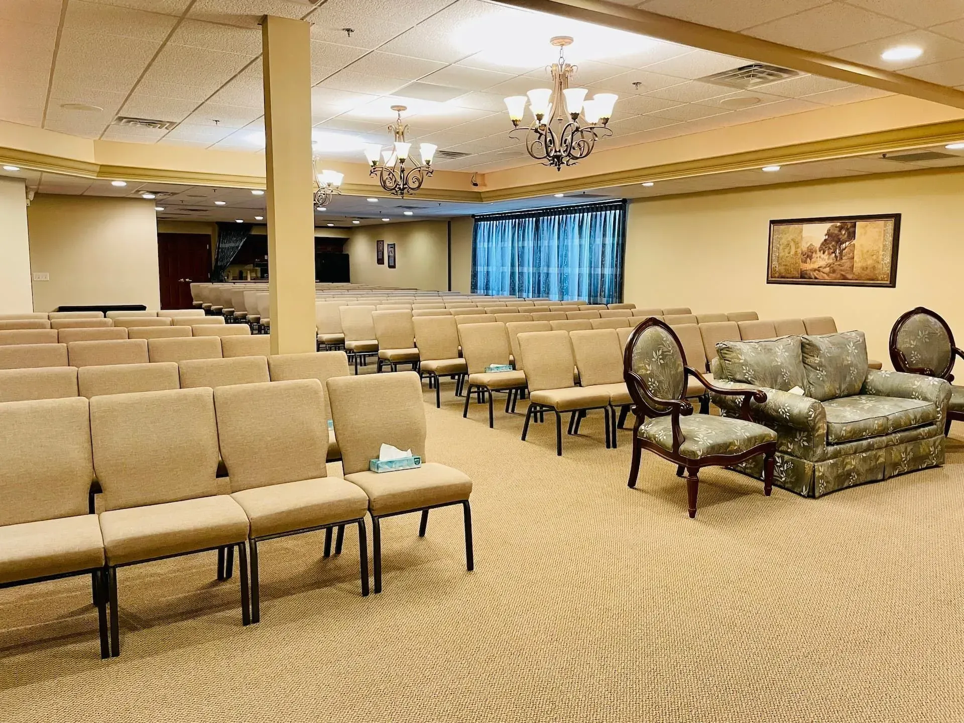 Empty banquet hall with beige chairs, chandeliers, and a patterned carpeted floor.