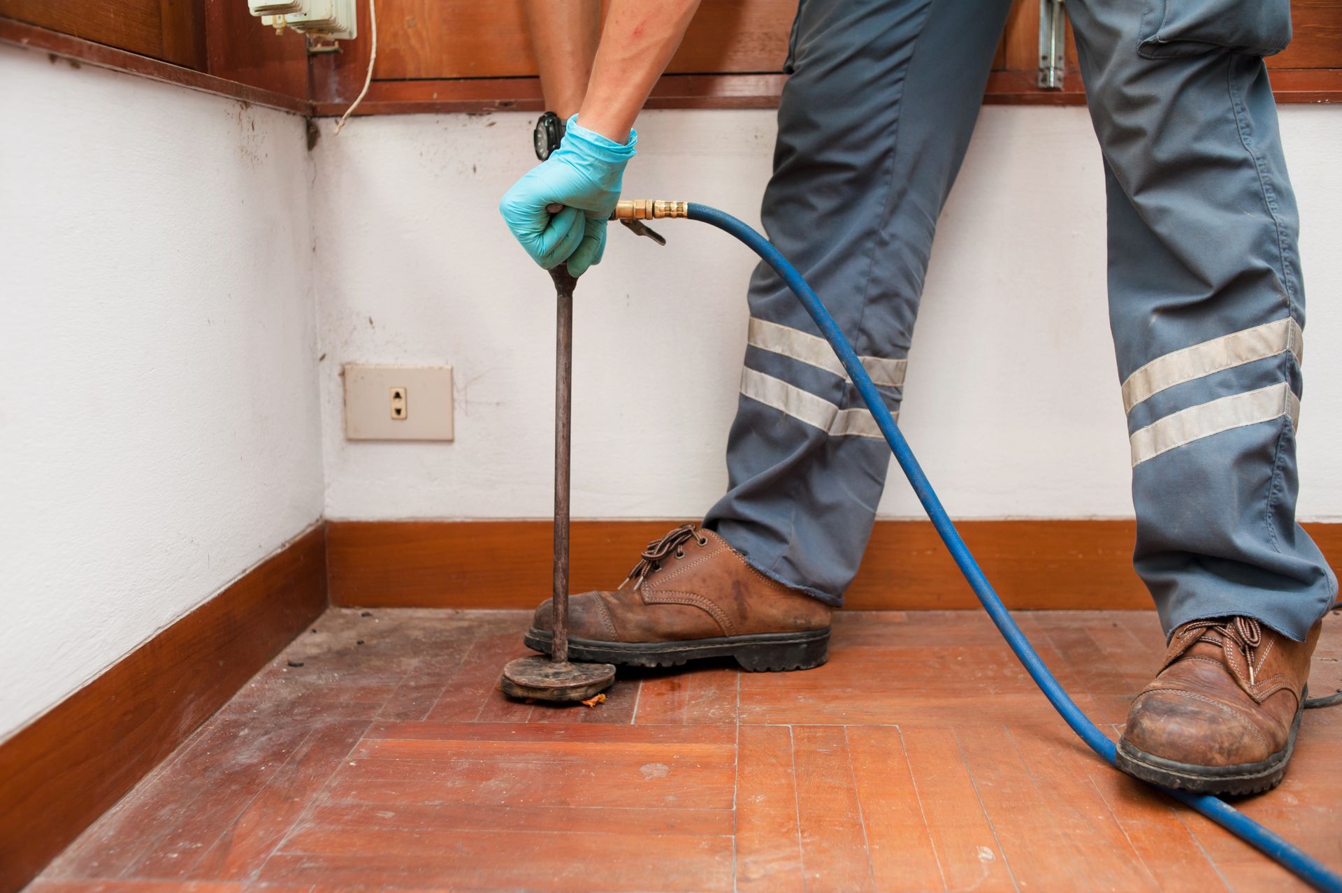 Pest control worker injecting insecticide near a wall and floor with wood paneling.