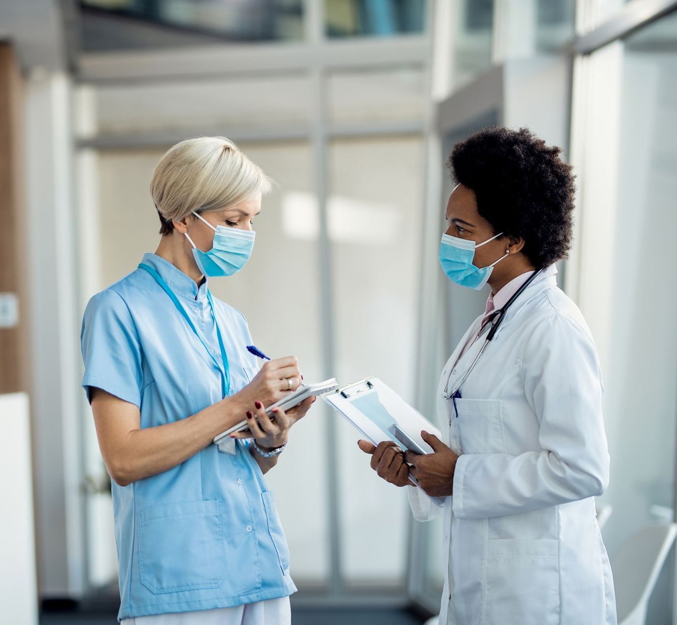 A nurse wearing a mask is talking to a doctor in a hospital.