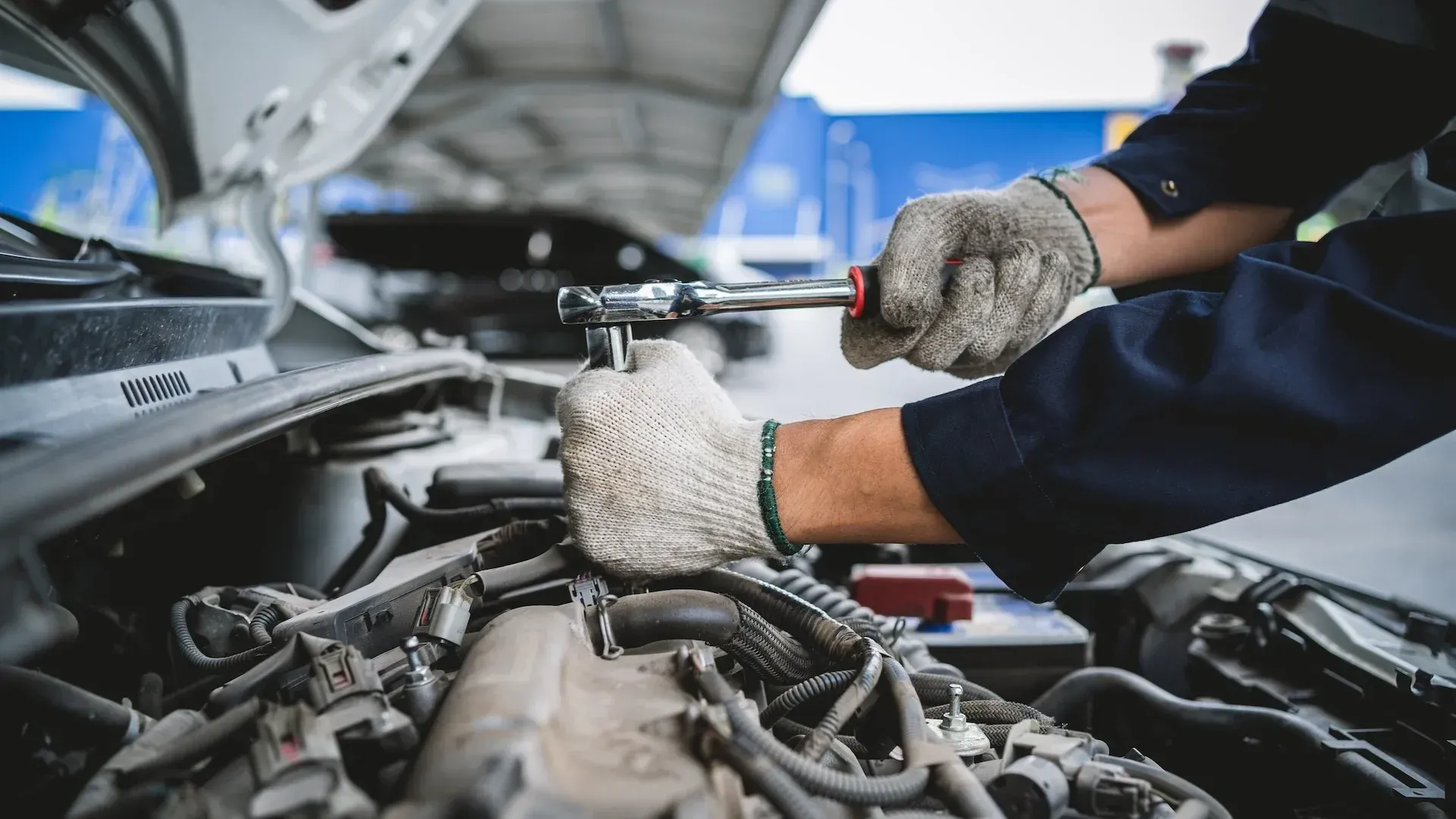 Mechanic wearing gloves working under an open car hood in a repair shop