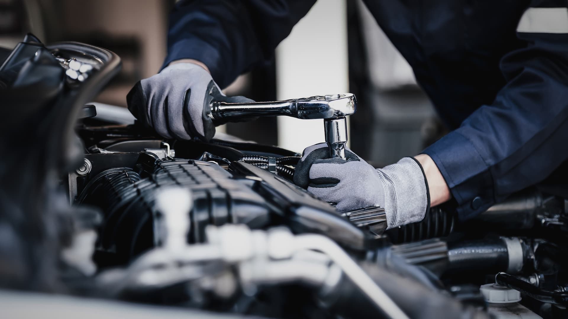 Gloved mechanic using a wrench to repair a car engine in a workshop