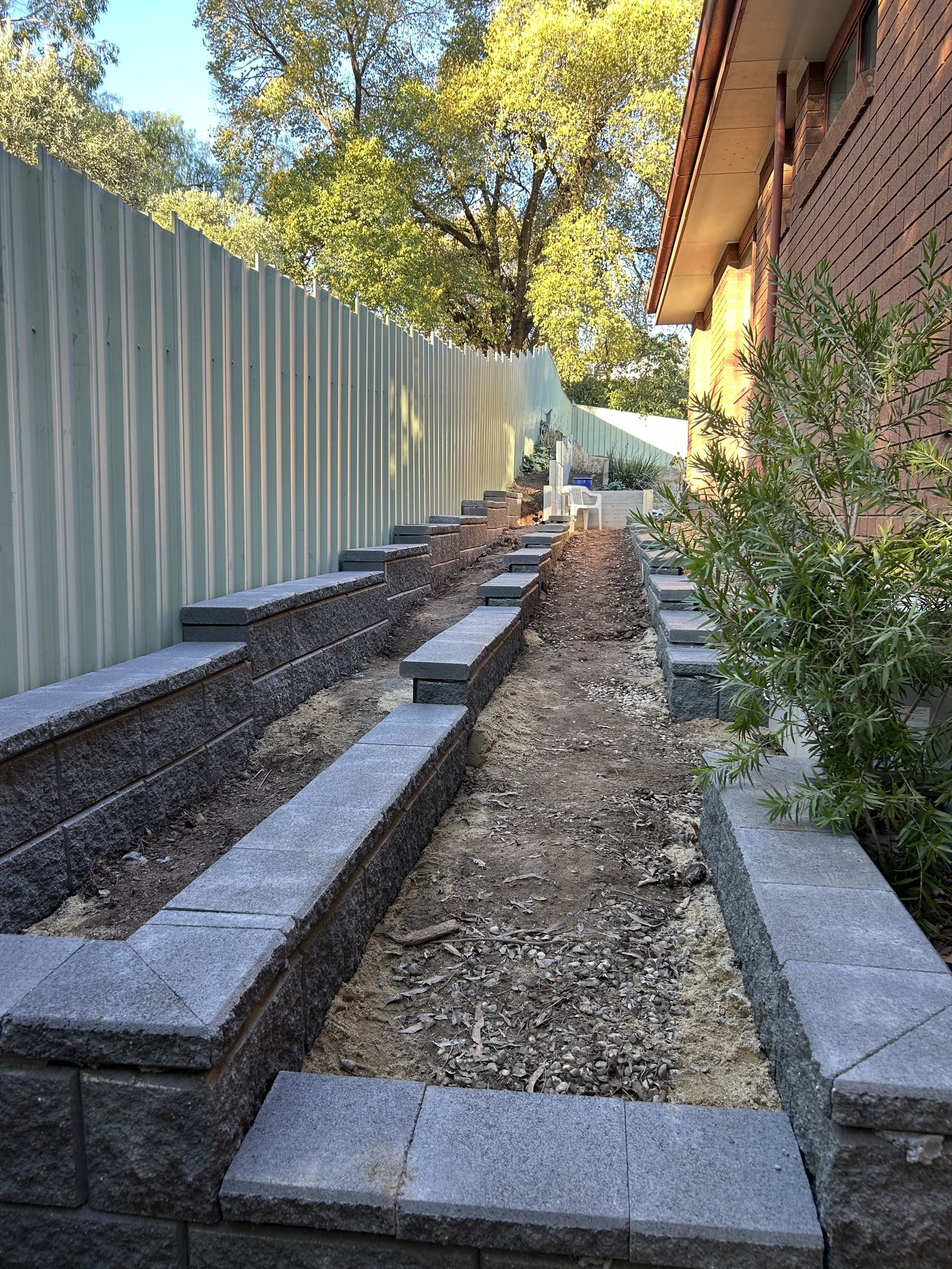 A narrow, dirt garden bed with grey retaining wall borders next to a building and fence — The Wright Way Building In North Albury, NSW