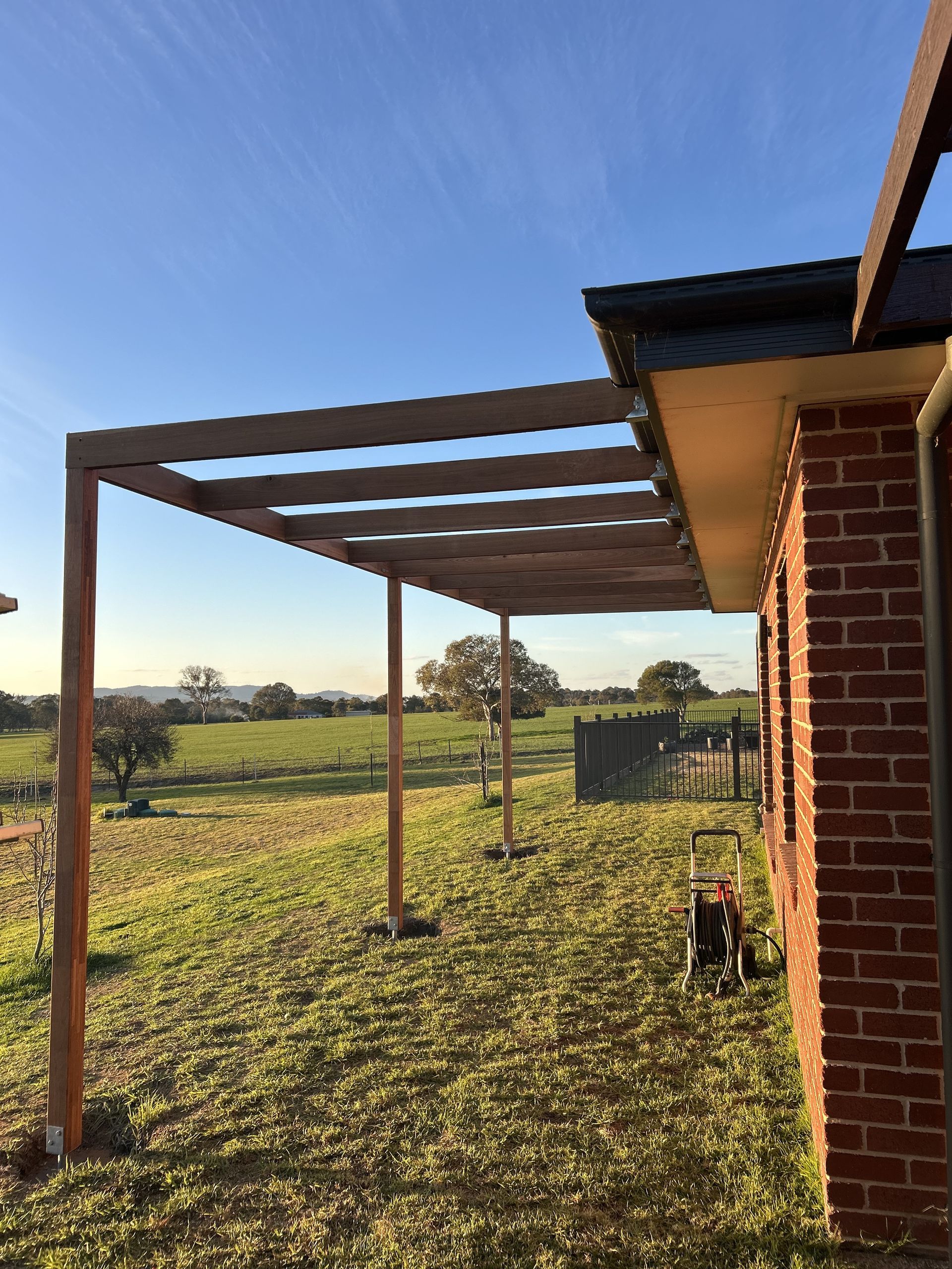 Pergola attached to a brick house, overlooking a grassy field under a blue sky — The Wright Way Building In North Albury, NSW