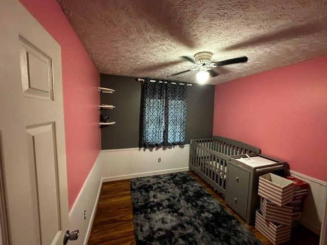 Small bedroom with pink walls, gray crib, patterned rug, and window with dark curtains.