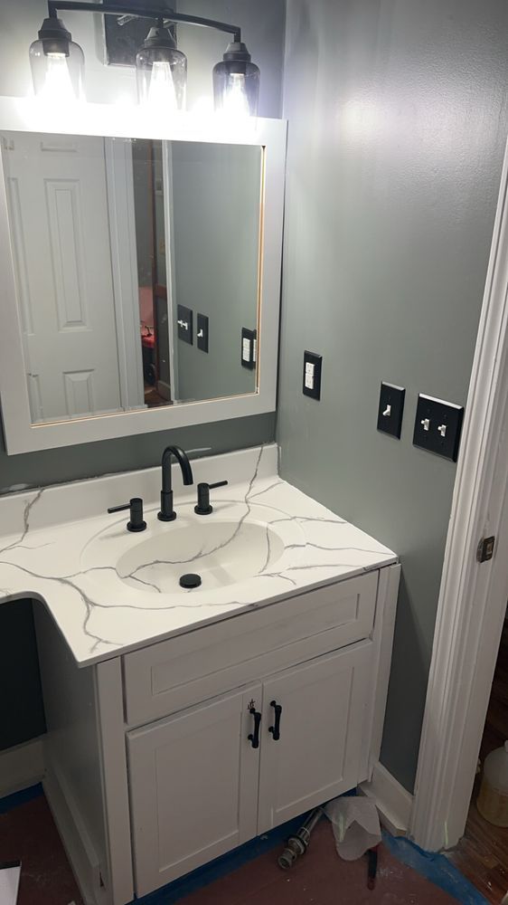 Modern bathroom vanity with mirror, black fixtures, gray walls, and vanity lights above sink.