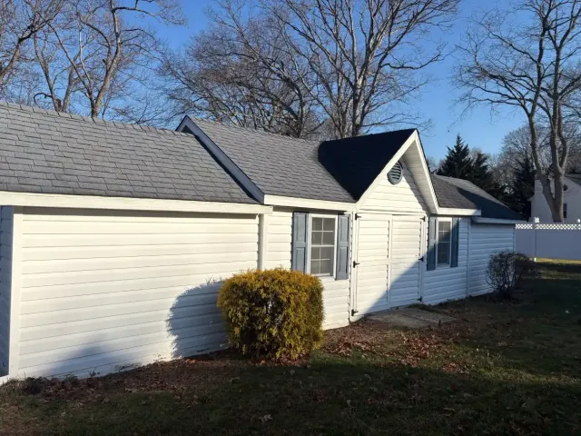Red industrial dumpster in a paved yard beside black trash bins and a building.