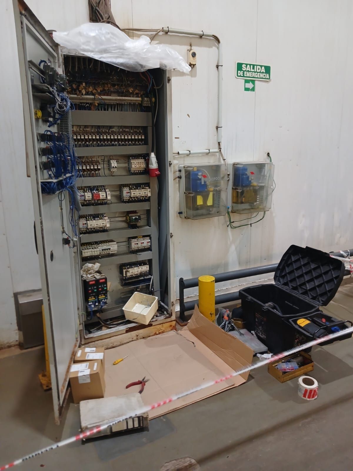 Armario eléctrico abierto con cableado, herramientas y piezas en el suelo en un área de mantenimiento.