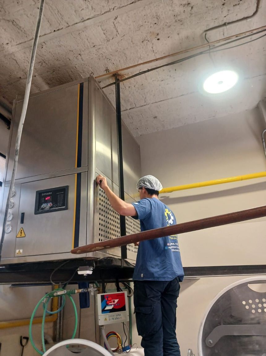 Obrero manejando una gran máquina industrial en una fábrica, con casco y camisa azul.