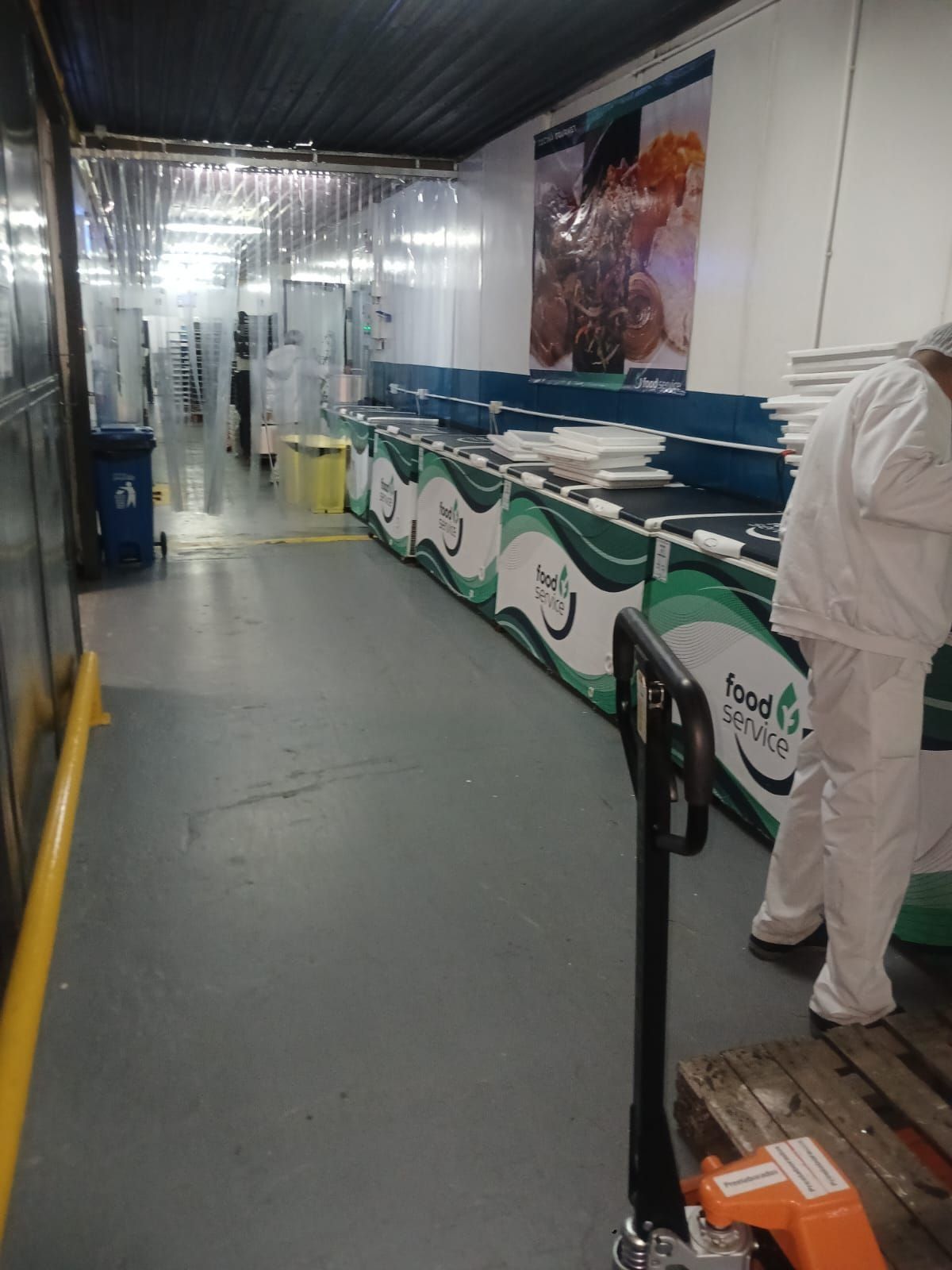 Zona de trabajo interior con una larga fila de contenedores de reciclaje verdes y una persona con un traje protector blanco.