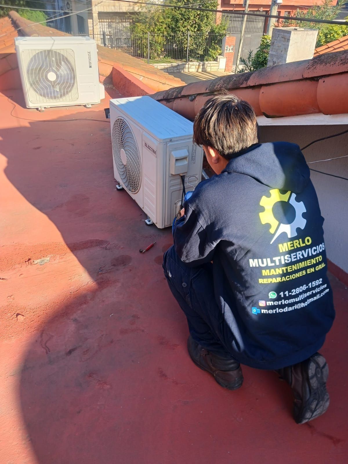 Un técnico trabaja arrodillado sobre un tejado rojo junto a las unidades exteriores de aire acondicionado