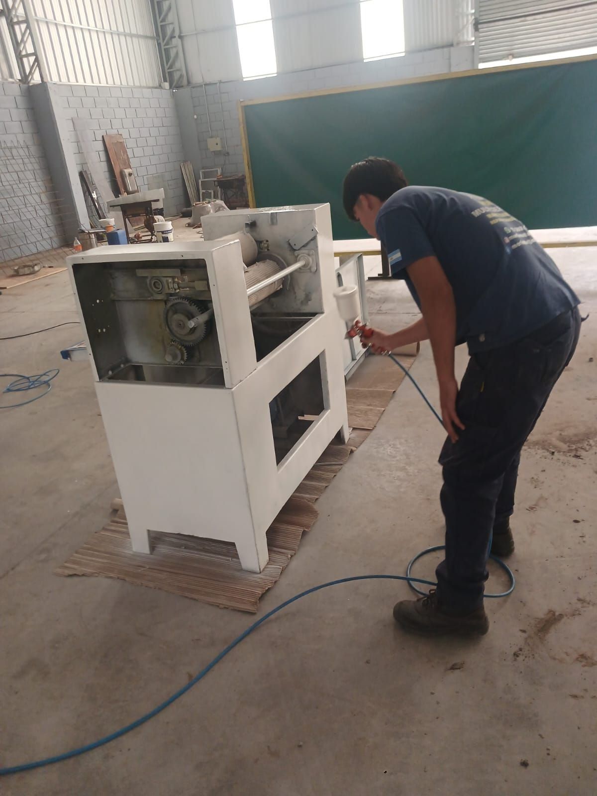 Un trabajador maneja una máquina industrial blanca en un taller, con mangueras y herramientas en el suelo.