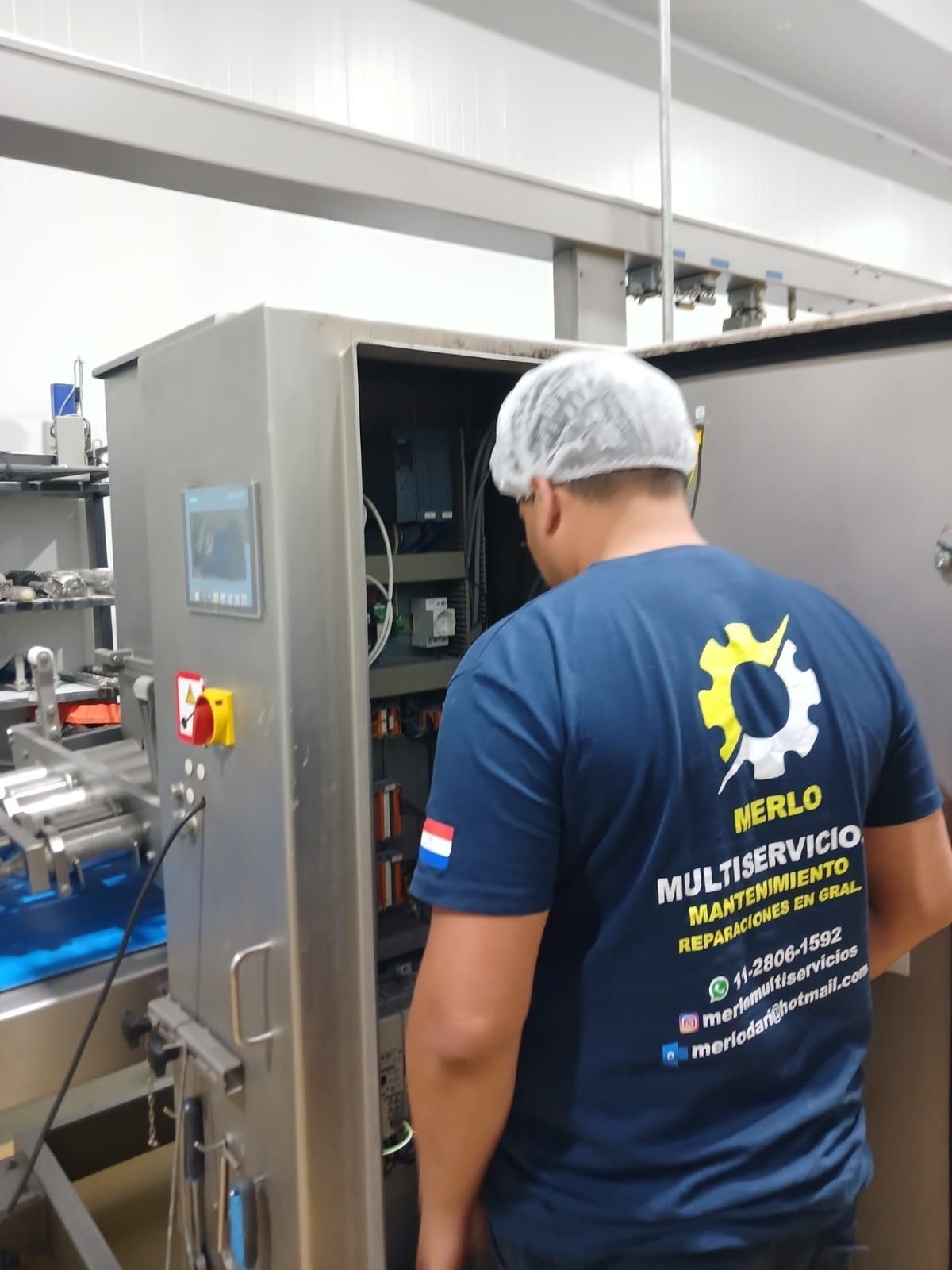 Técnico con camisa azul inspeccionando equipos industriales abiertos en un taller.