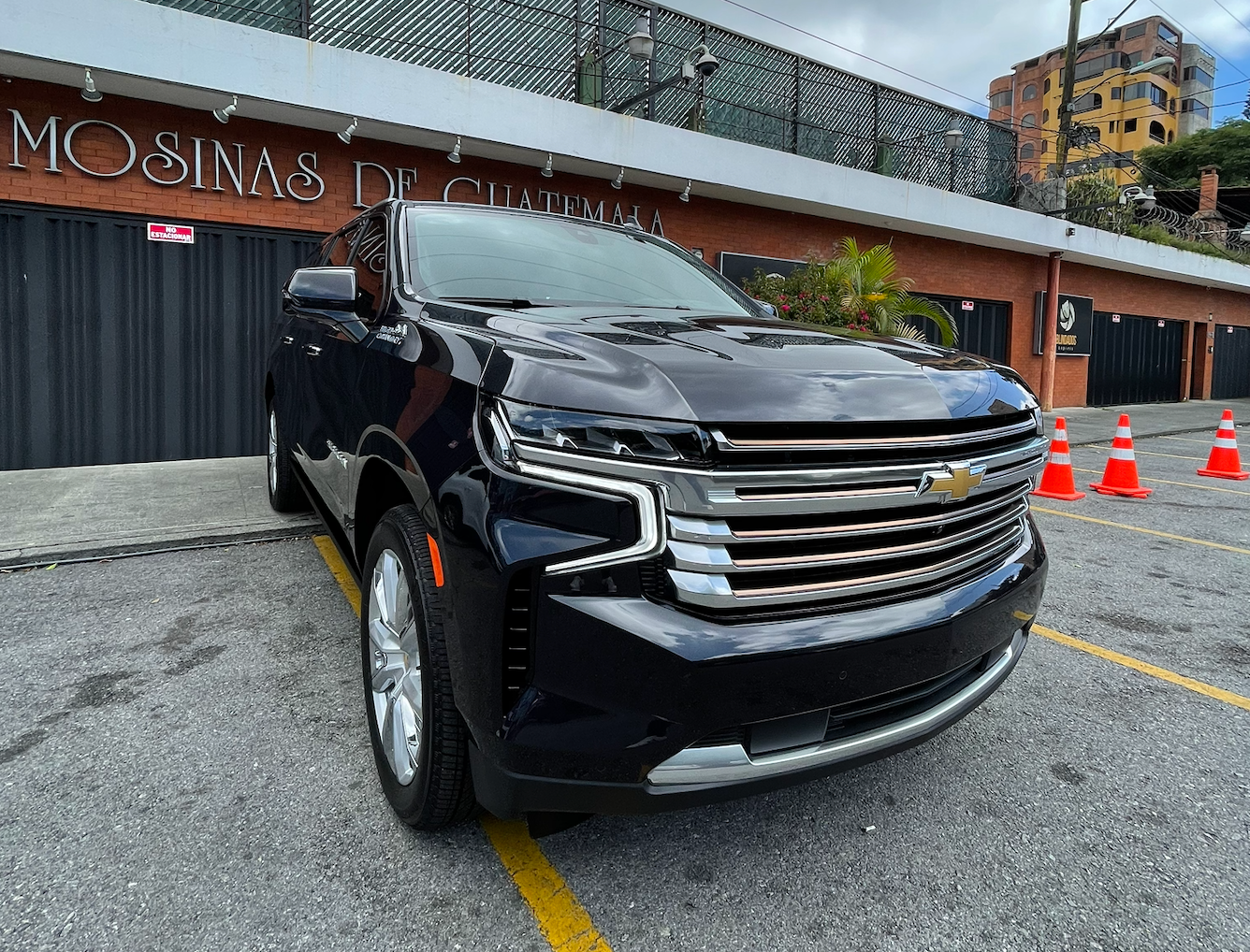 Un SUV negro estacionado frente a un edificio en una calle mojada, con conos naranjas cerca.