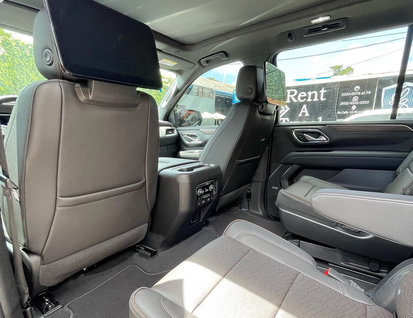 Interior de un coche de lujo con asientos de cuero negro y gris y una consola central, visto desde el asiento trasero.