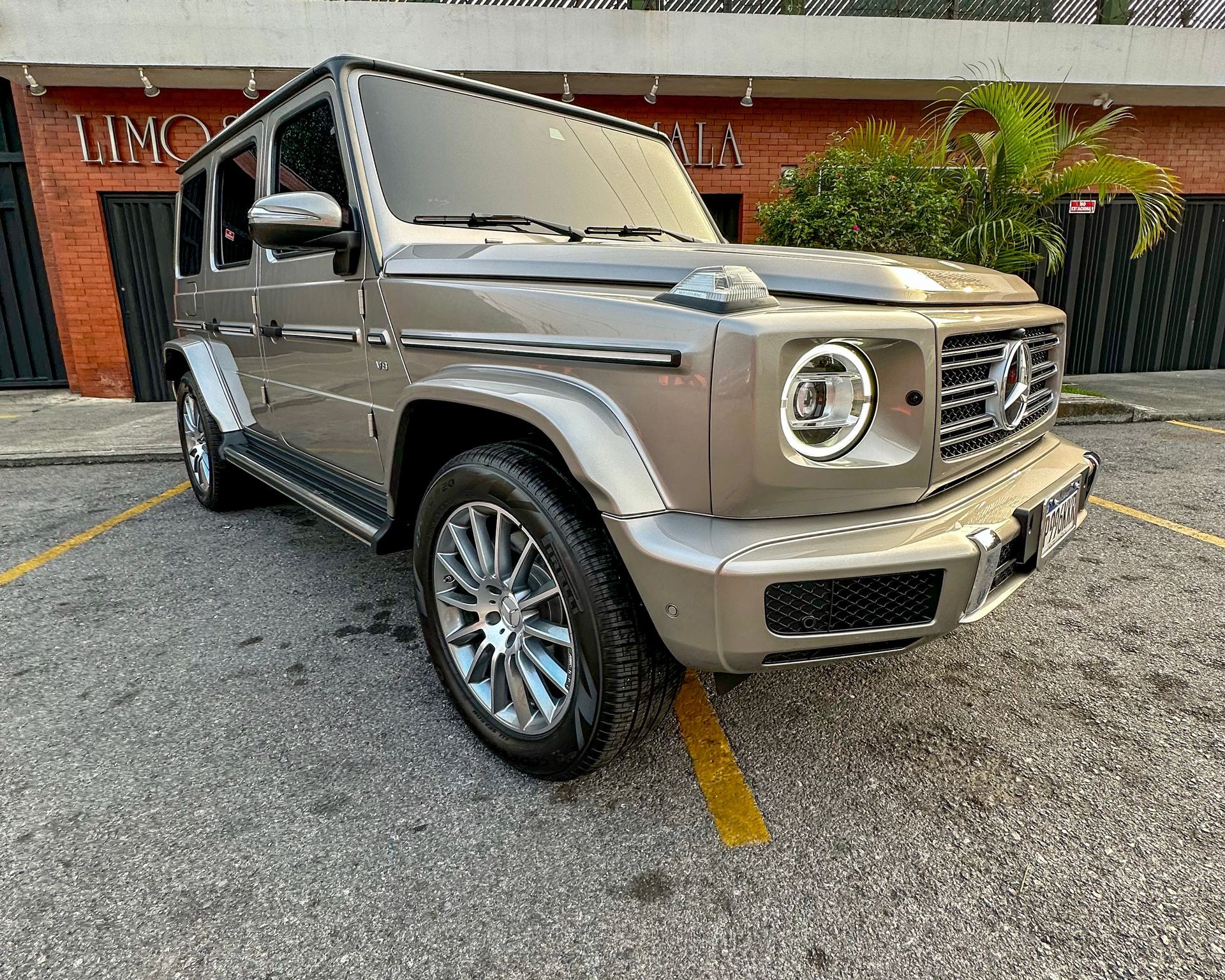Un SUV Mercedes-Benz Clase G de color beige estacionado en la acera frente a un edificio.