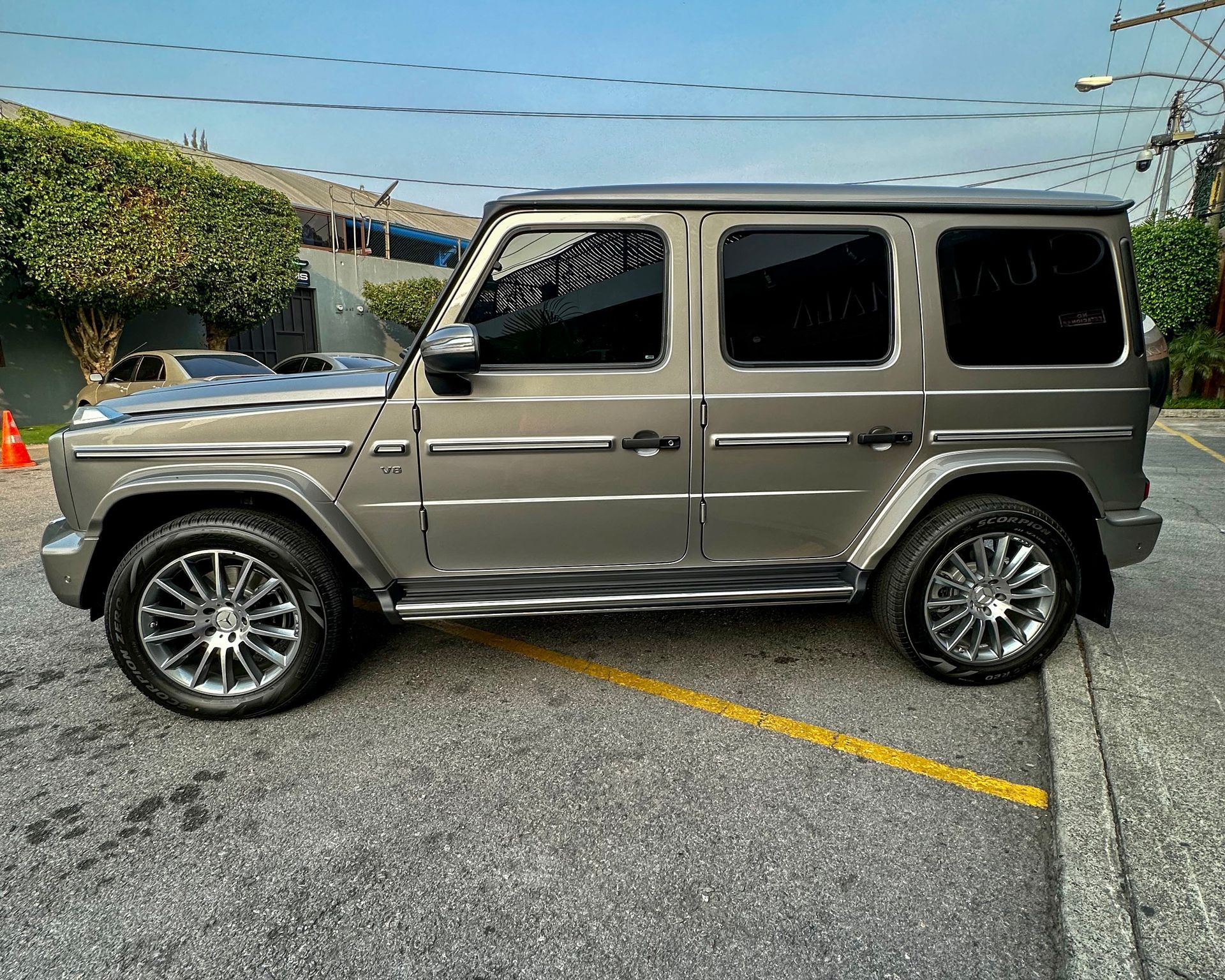 SUV Mercedes Clase G plateado estacionado en un aparcamiento, vista lateral en un día soleado.