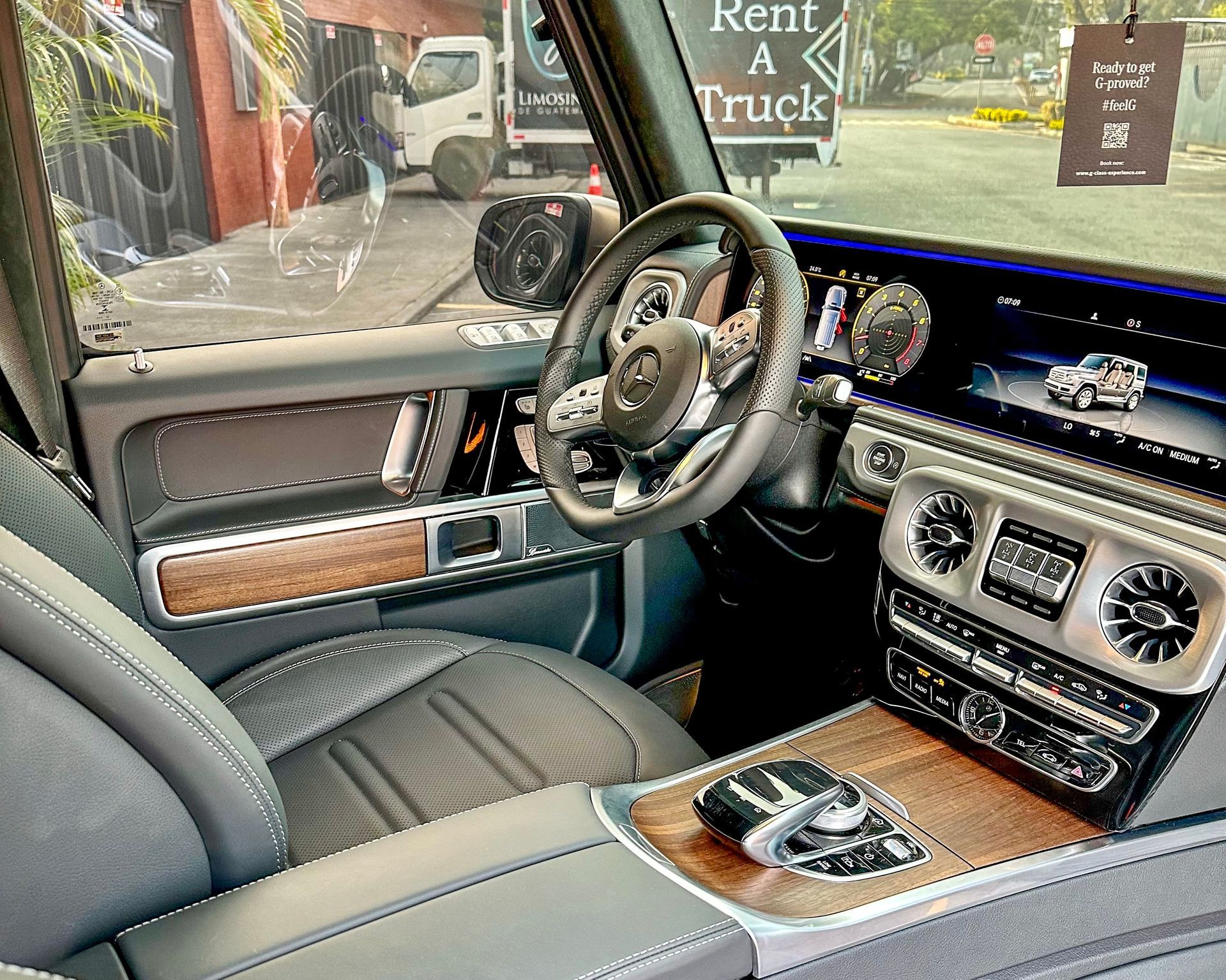 Interior de coche de lujo con asientos de cuero gris, detalles en madera y salpicadero digital.