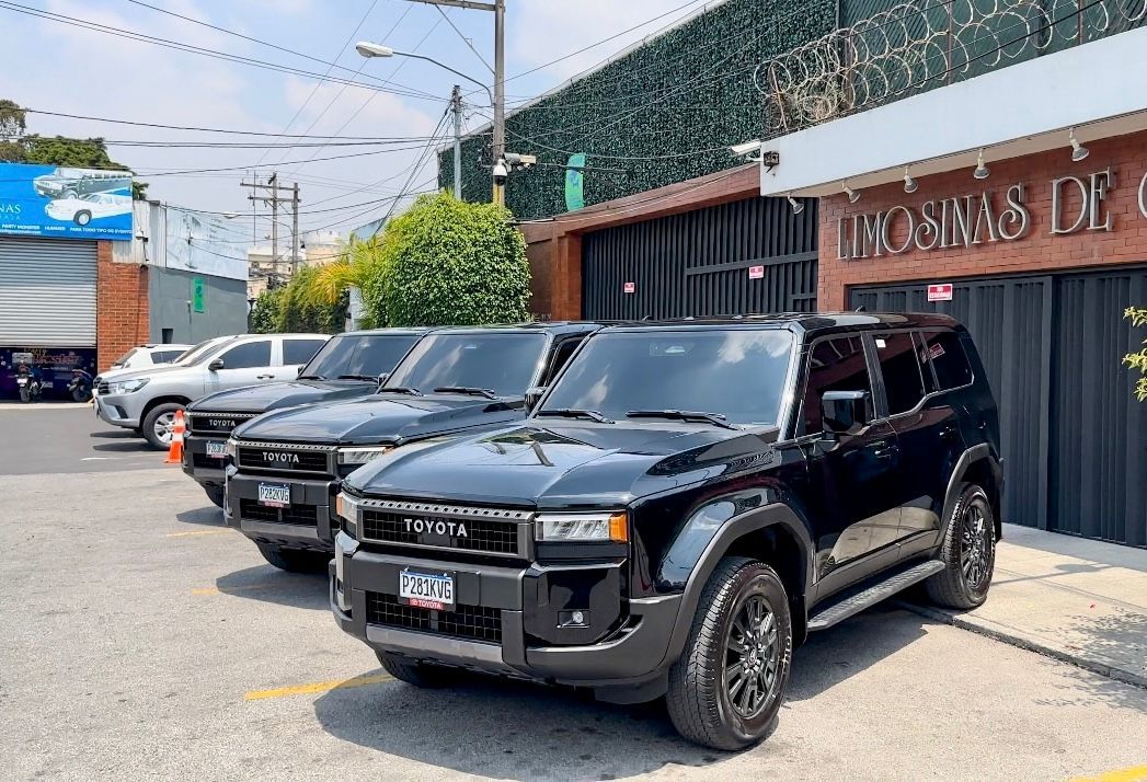 Tres camionetas SUV negras estacionadas en una calle junto a un edificio.