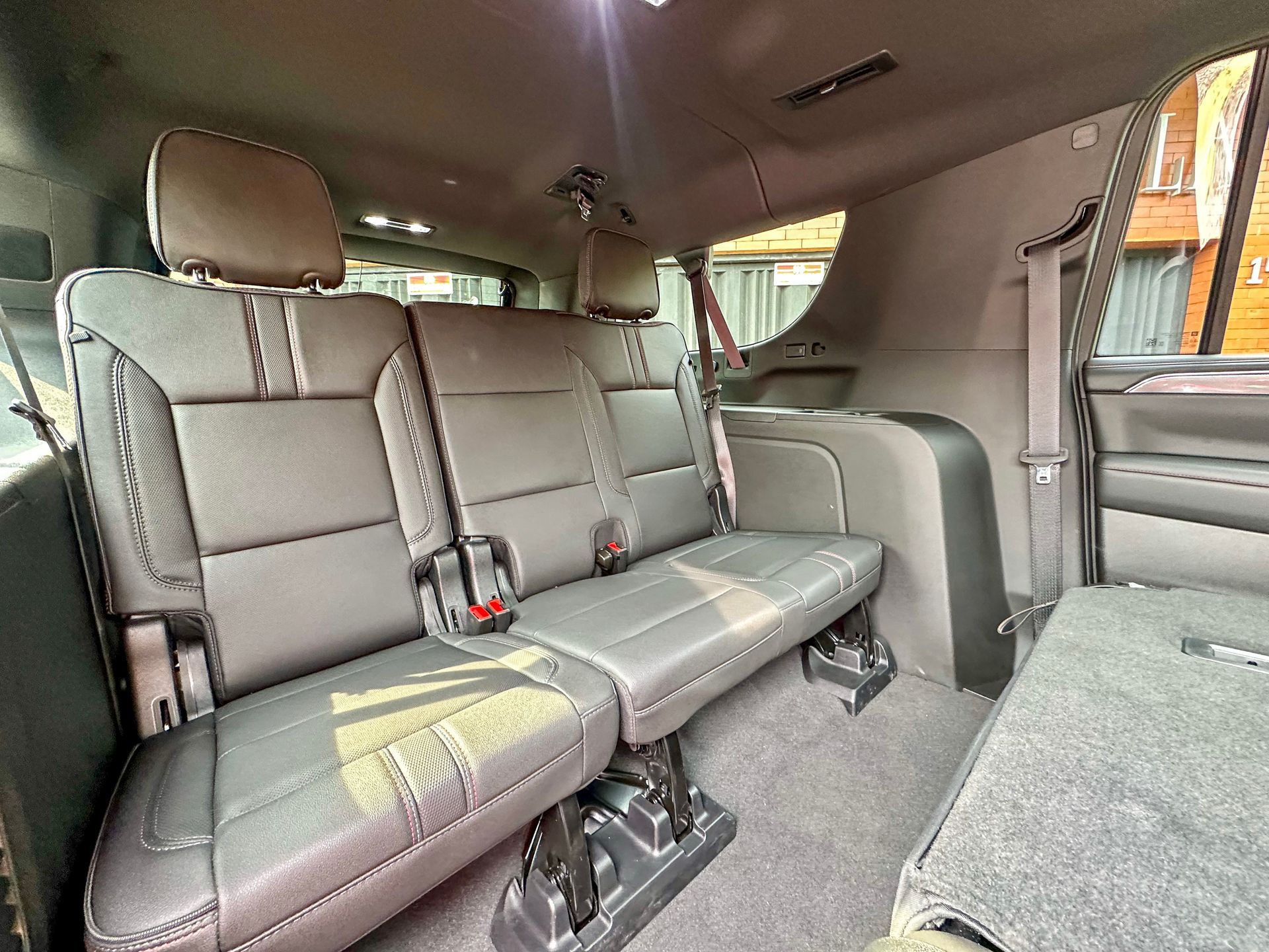 Interior trasero de una minivan con asientos corridos de cuero gris y reposabrazos plegados.