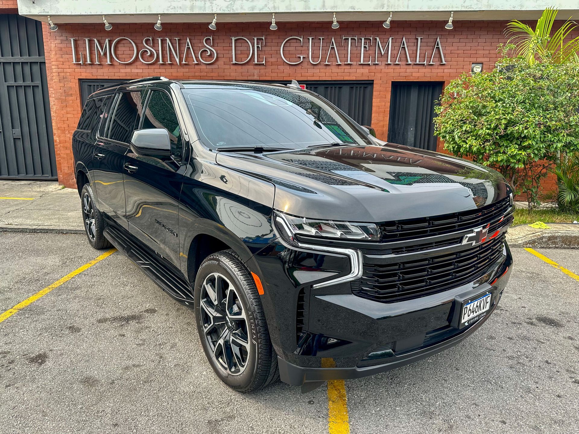 Una camioneta SUV negra estacionada frente a un edificio con un letrero de madera que dice “Limousinas de Guatemala”.