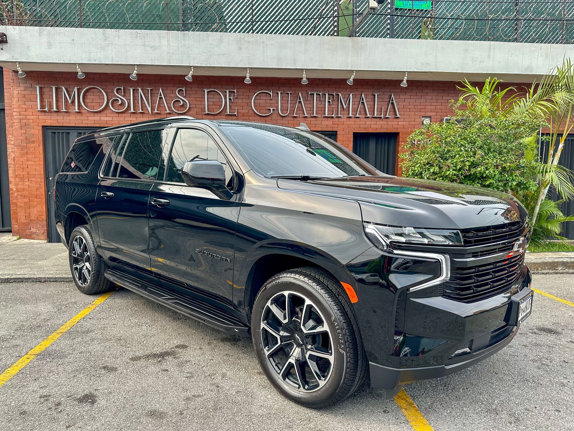 Un SUV negro estacionado frente a un edificio de servicio de limusinas con letrero en español.
