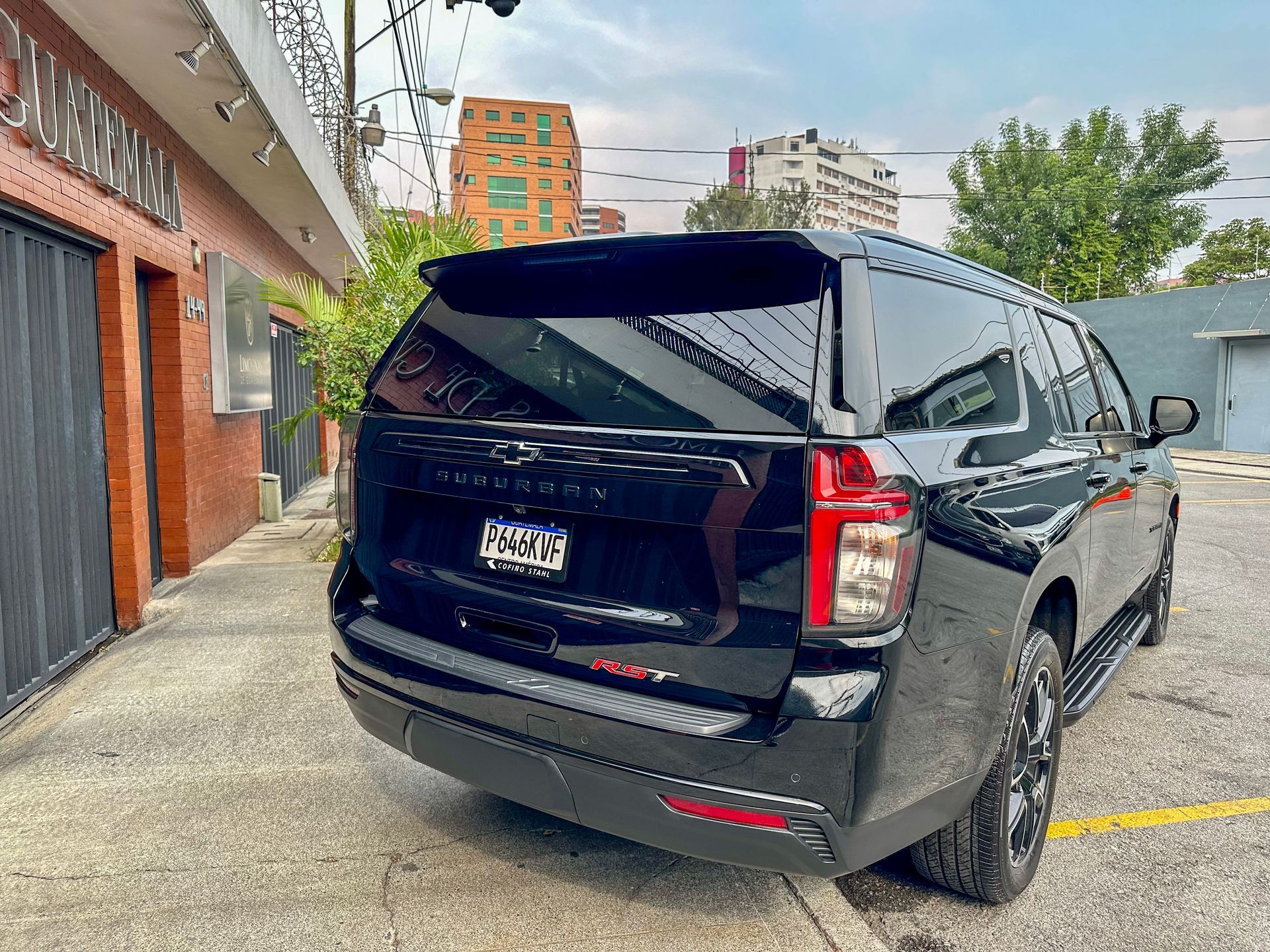 Un SUV negro estacionado junto a un edificio de ladrillos en una acera de un estacionamiento urbano.