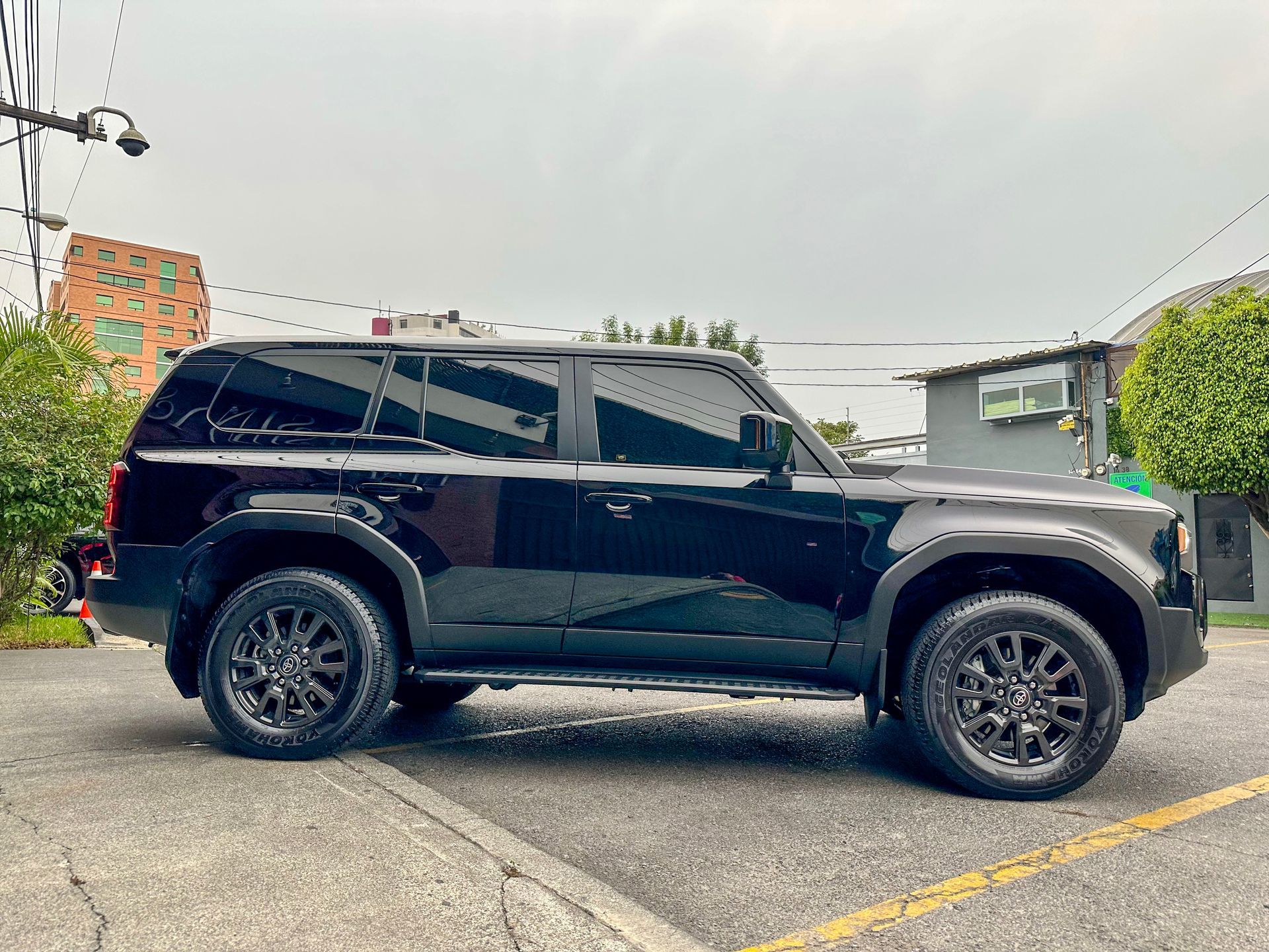 SUV negro estacionado en la entrada de una casa, visto de lado bajo un cielo nublado.