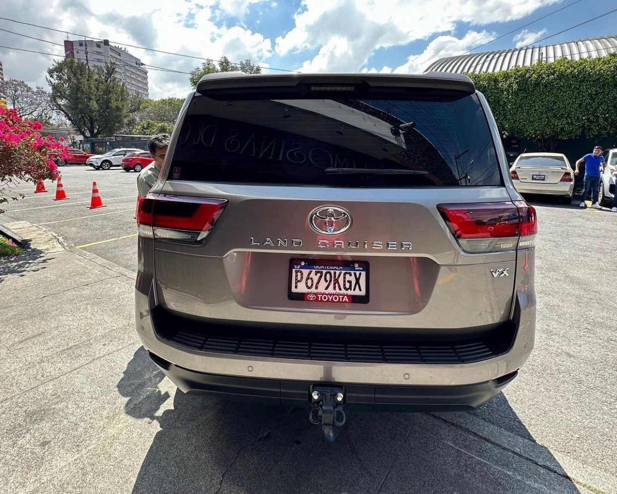 Vista trasera de un SUV Toyota gris estacionado en un aparcamiento con conos naranjas y árboles al fondo.