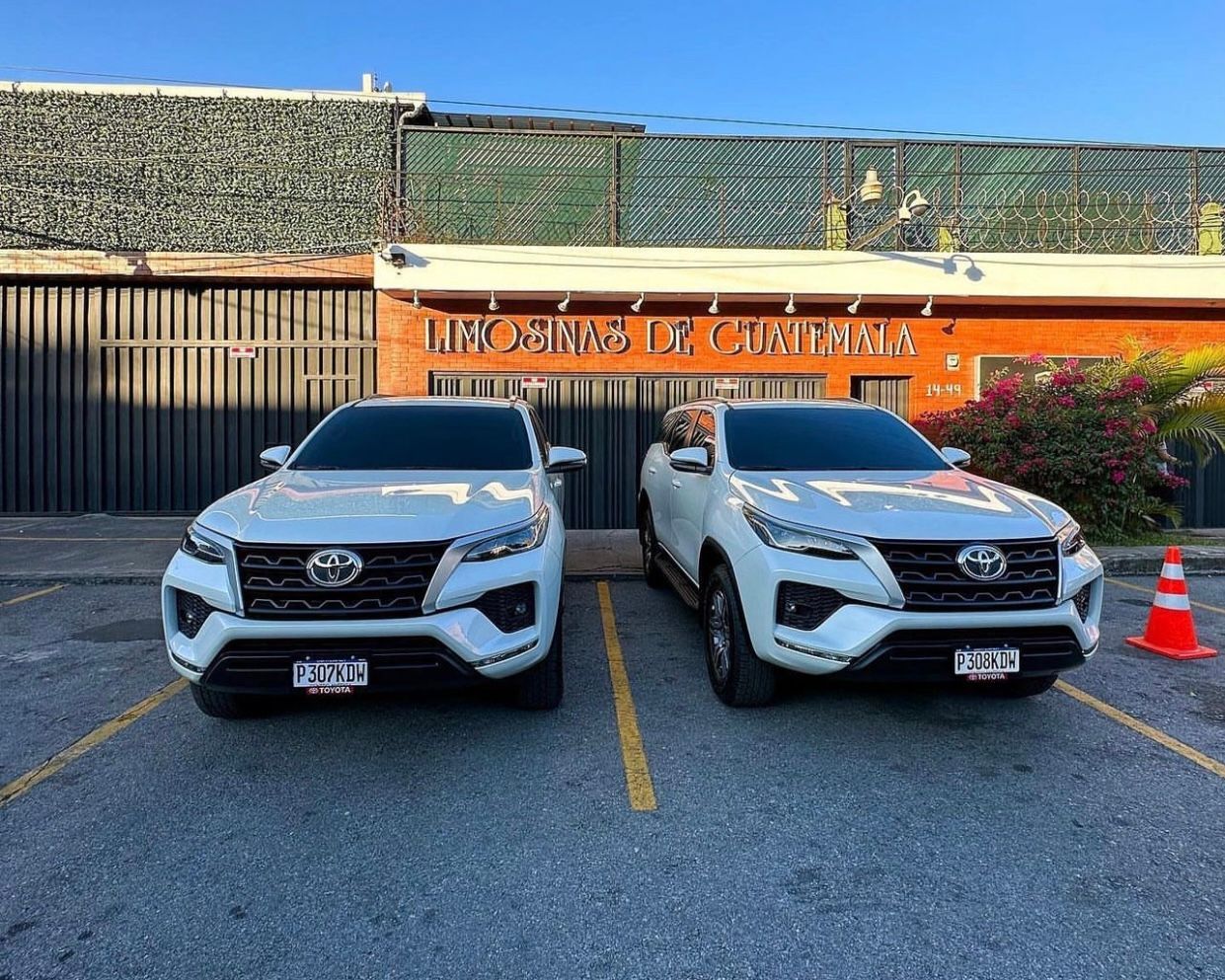 Dos camionetas Toyota blancas estacionadas una al lado de la otra frente a un edificio con letreros naranjas.