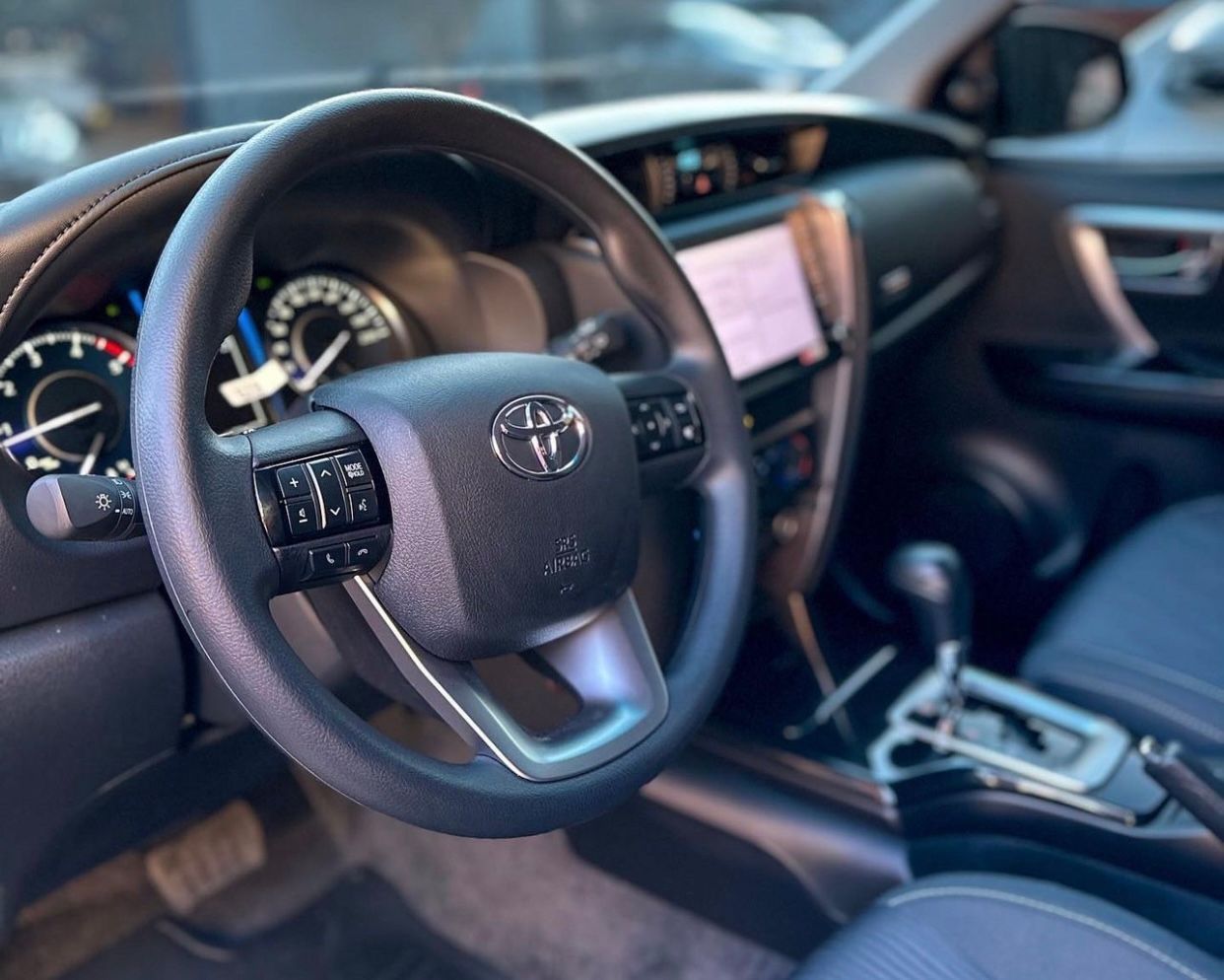 Interior de un automóvil Toyota con volante, tablero, pantalla central y asientos de cuero.