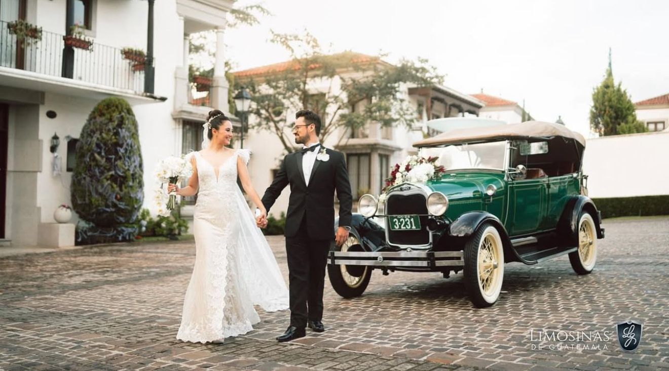 Los novios caminan junto a un coche verde antiguo frente a una villa blanca.