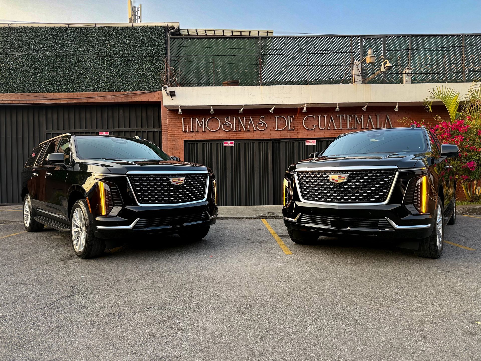 Dos camionetas SUV negras estacionadas frente a un edificio con fachada y letrero de estilo español.