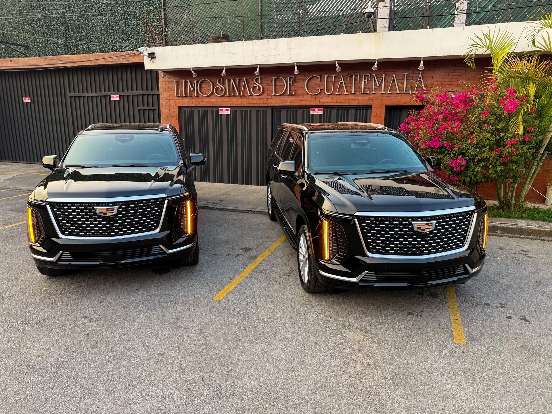 Dos camionetas Cadillac negras estaban estacionadas una al lado de la otra frente a la entrada de un hotel con flores