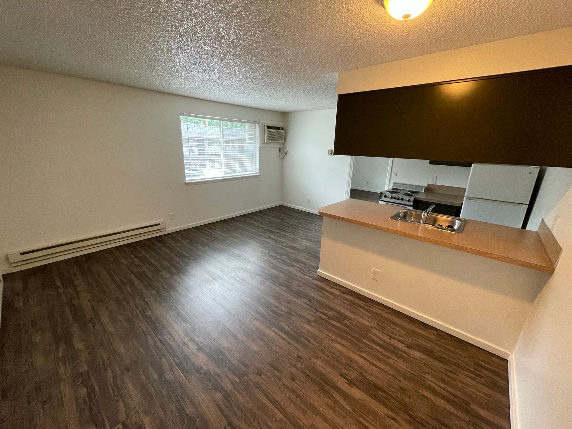 Empty apartment living space with wood-look flooring, breakfast bar, and window.