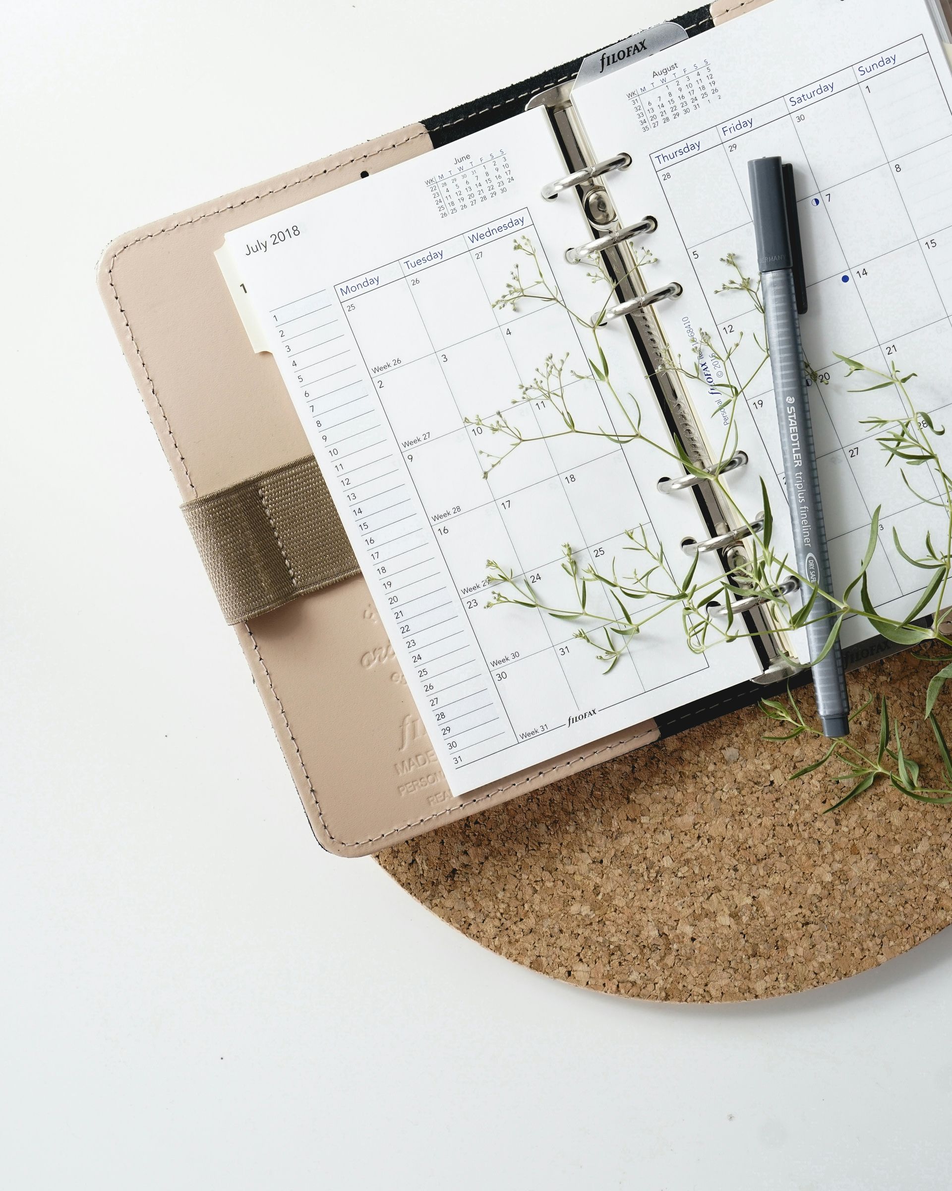 a notebook with a pen and flowers on it is sitting on a cork mat .