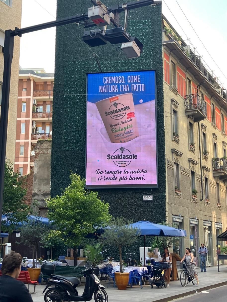Scena di strada con un grande cartellone pubblicitario rosa su un edificio in mattoni sopra un caffè all'aperto.