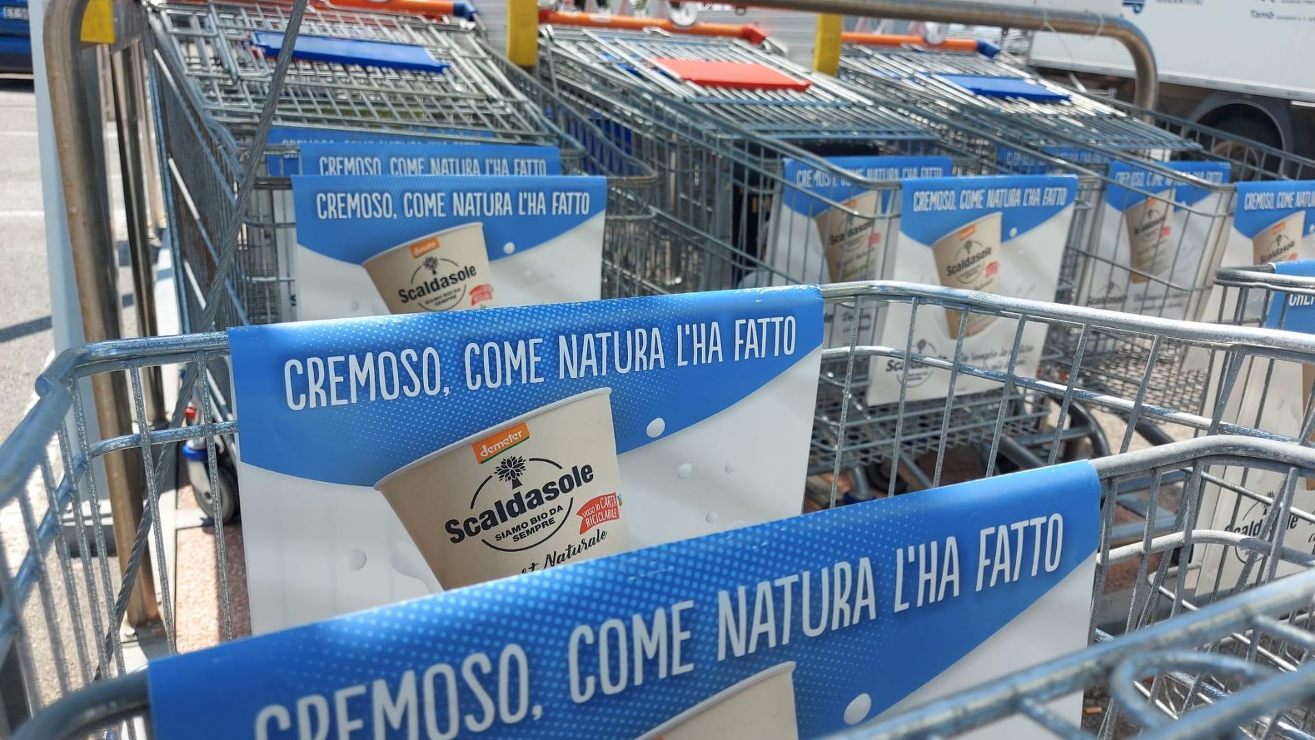 Carrelli della spesa con cartelli blu che indicano confezioni di formaggio italiano in una corsia di un supermercato.